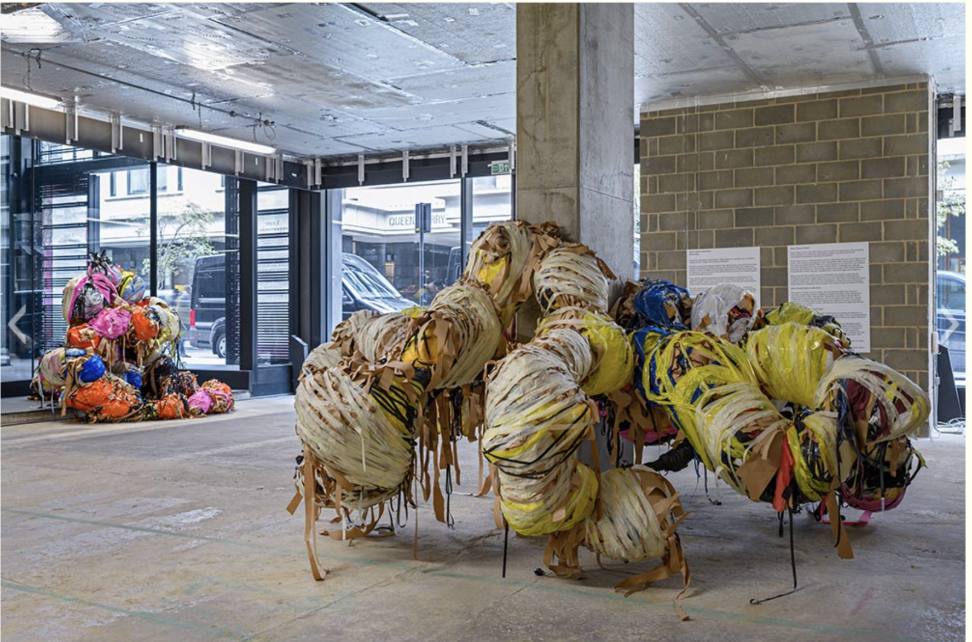 Contemporary art installation of large, colorful, abstract sculptures made of fabric and wire displayed in an unfinished art gallery