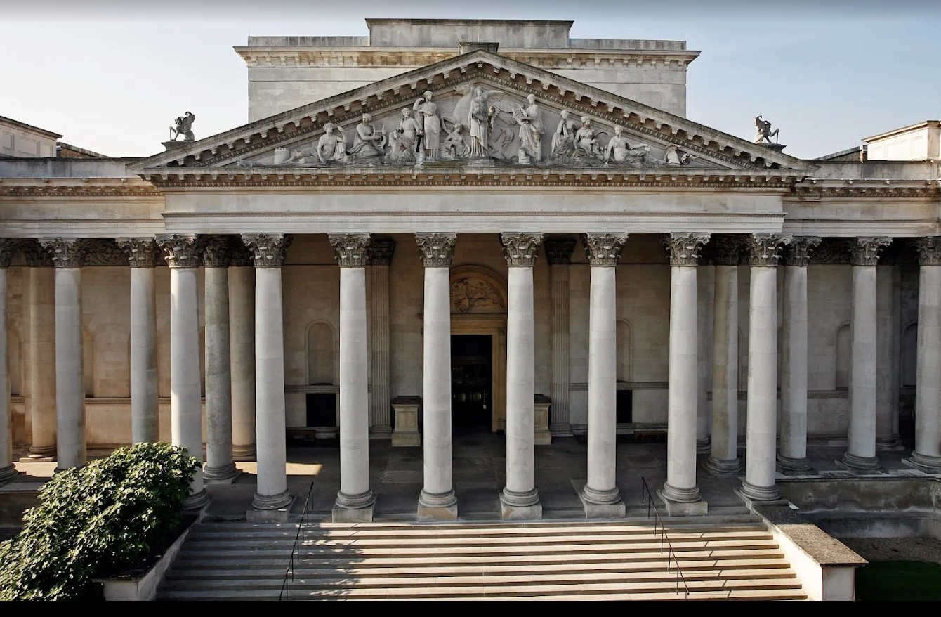 Front view of a historic Greek-style building with large white columns, marble statues, and intricate sculptures on the pediment.