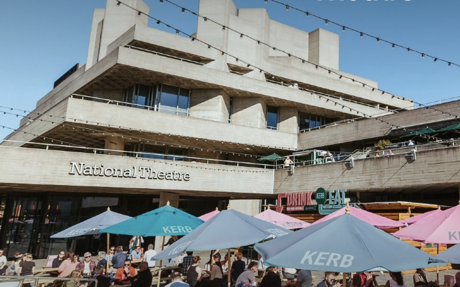 People dining outdoors with umbrellas in front of a large modern concrete building labeled 'National Theatre' on a sunny day.