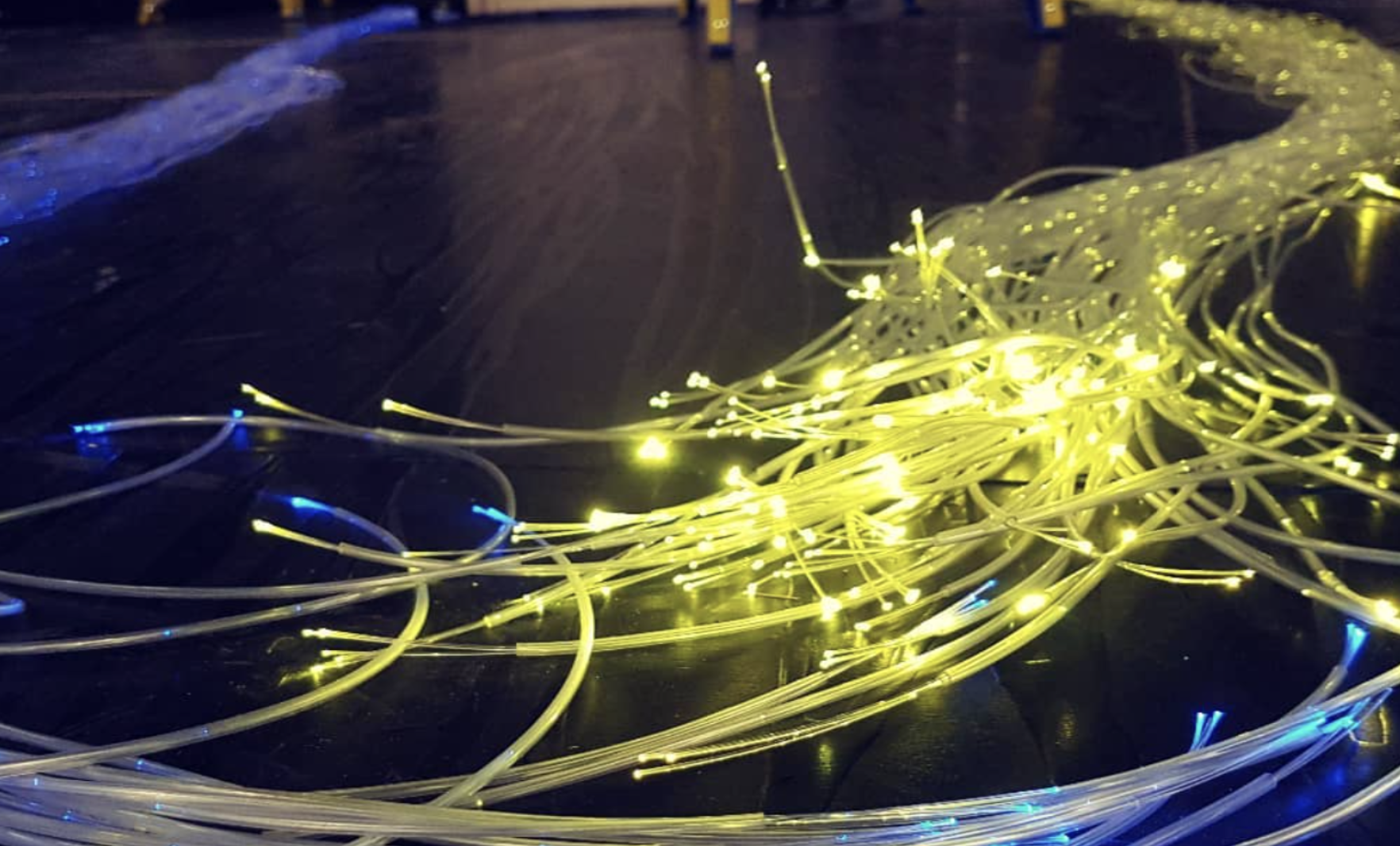 Yellow and blue illuminated string lights tangled on a dark floor.