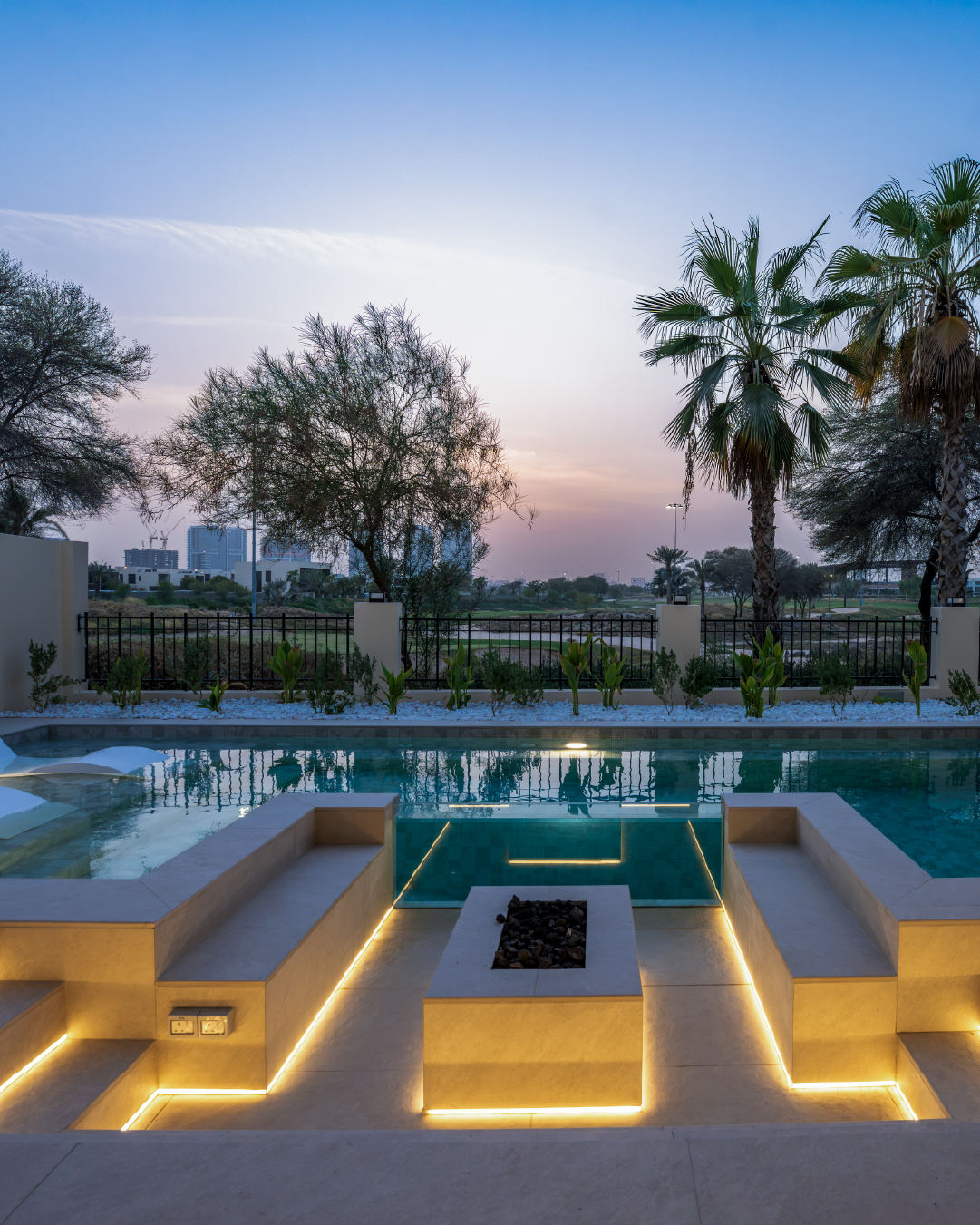 Dubai villa pool terrace at sunset with landscaped garden, outdoor seating and integrated lighting.