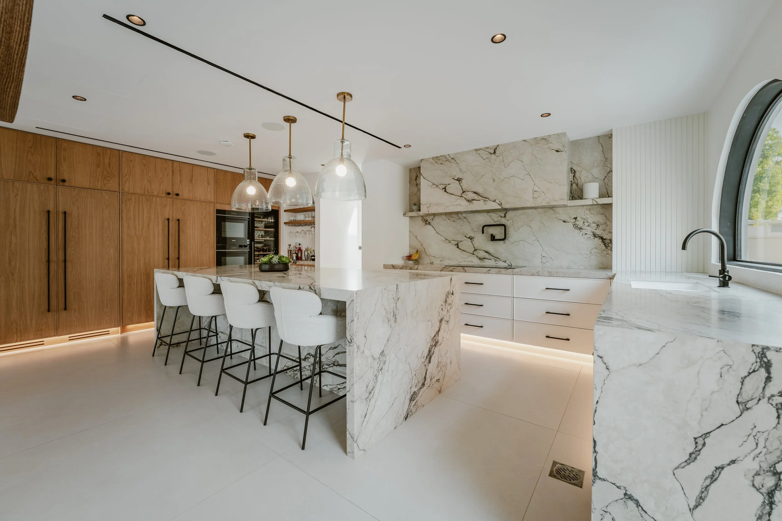 Al Mahra Arabian Ranches villa kitchen with marble island, timber cabinetry, pendant lights and bar seating.