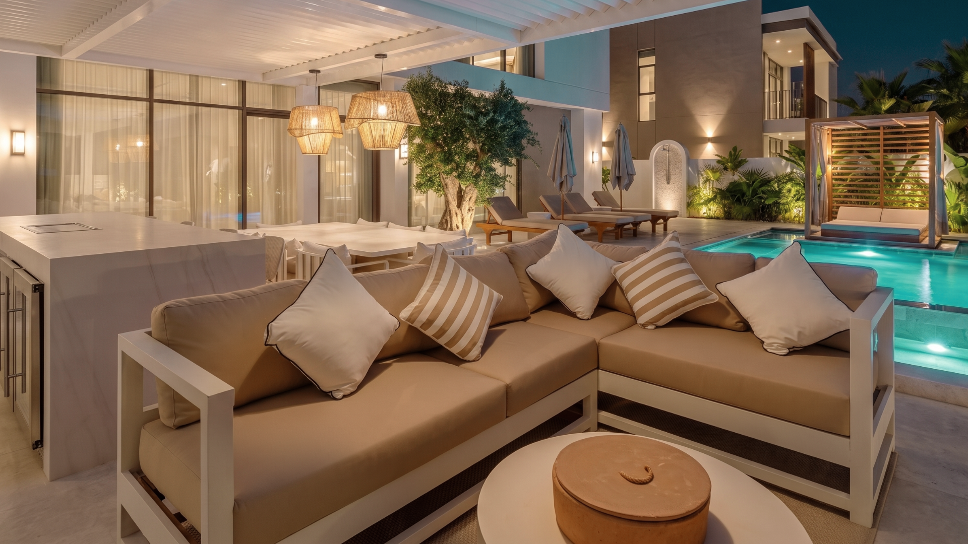 Covered outdoor lounge beside an illuminated villa pool and landscaped garden in Tilal Al Furjan.