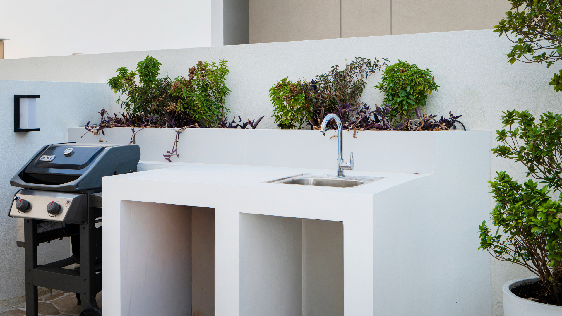 Bespoke outdoor counter with sink, barbecue and planted backdrop in a landscaped Dubai villa garden.
