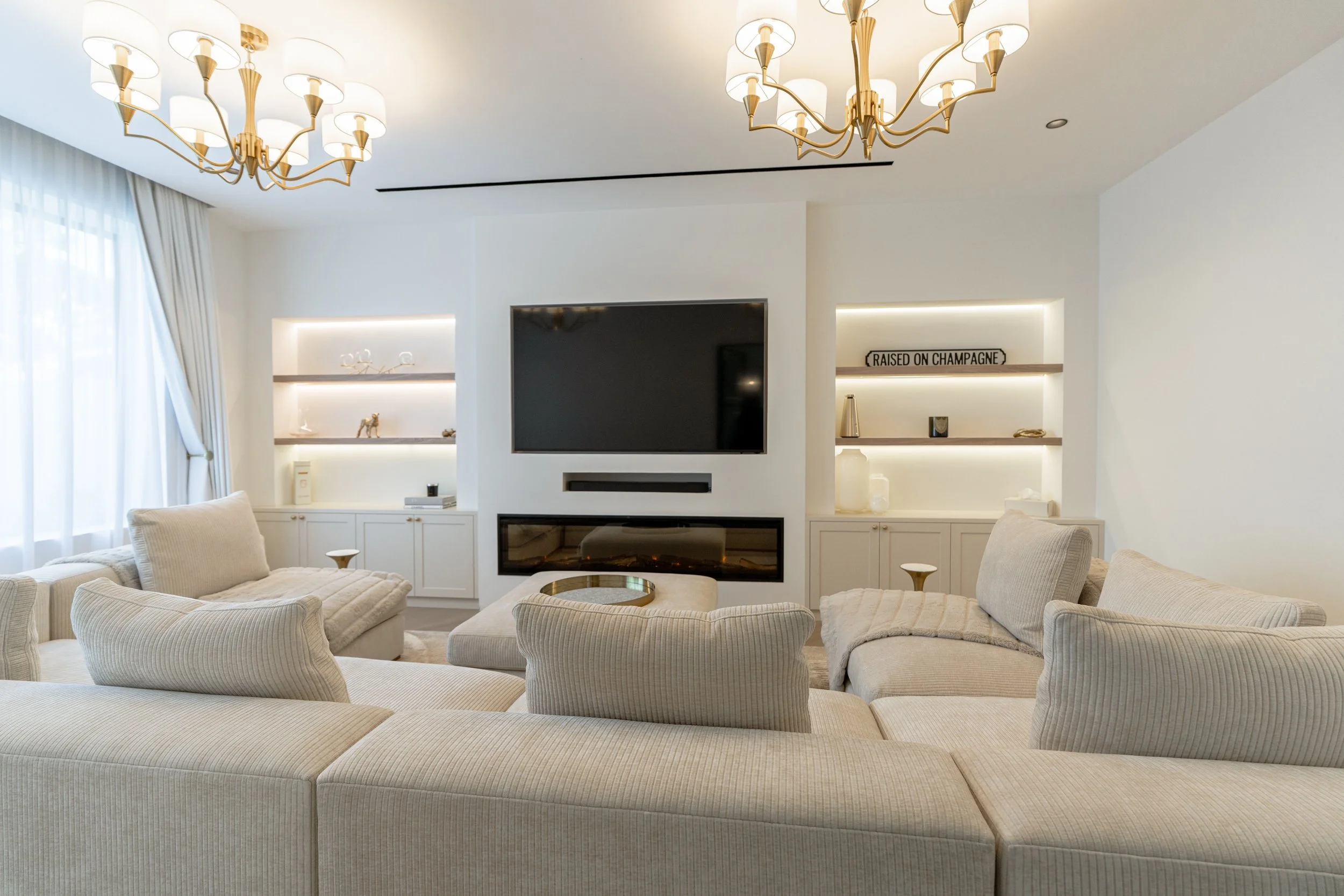 Jumeirah Park villa living room with neutral seating, custom media wall, built-in shelving and chandelier lighting.
