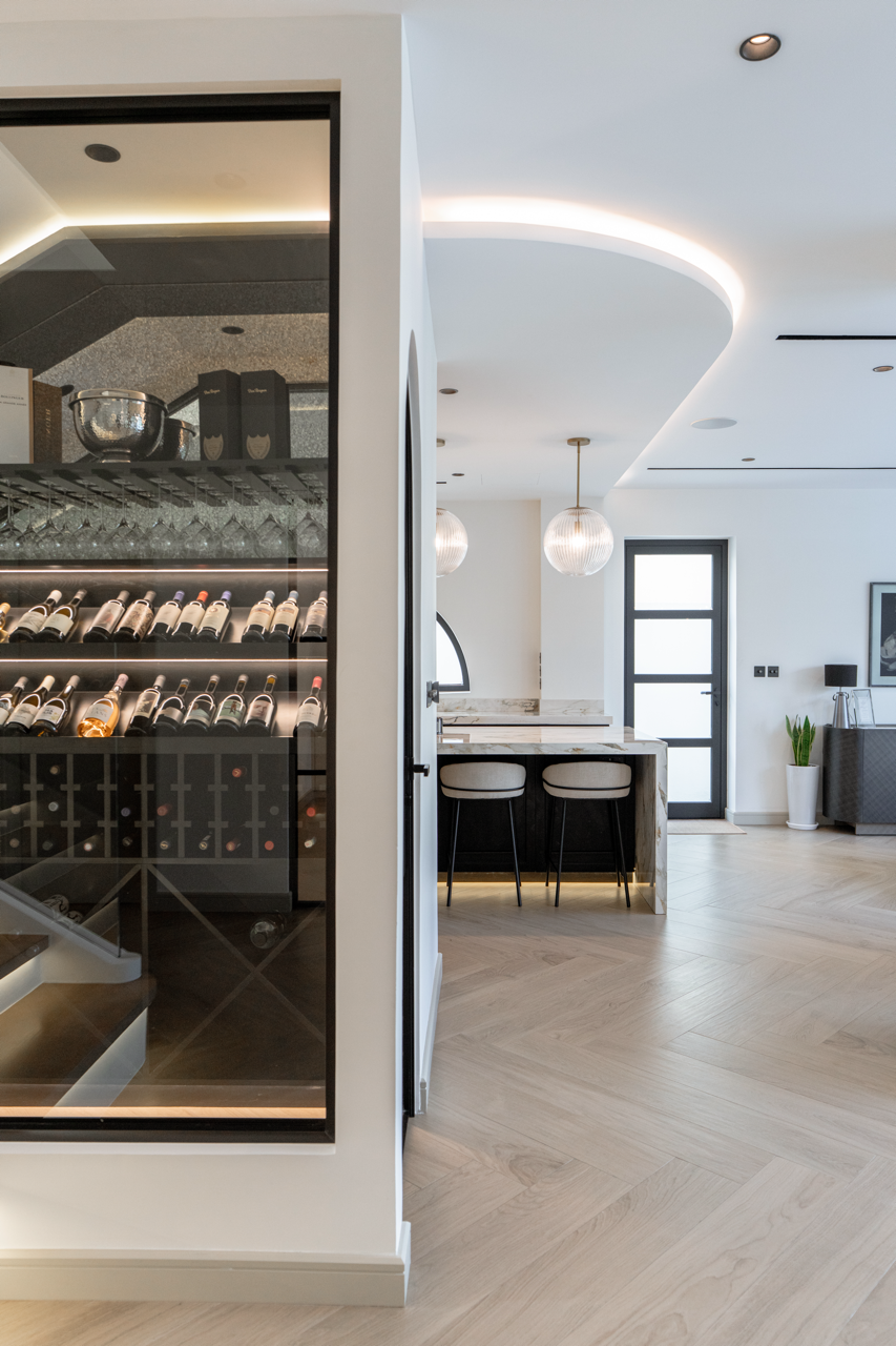 Glass-enclosed wine room beside an open-plan kitchen in a renovated Jumeirah Park villa.