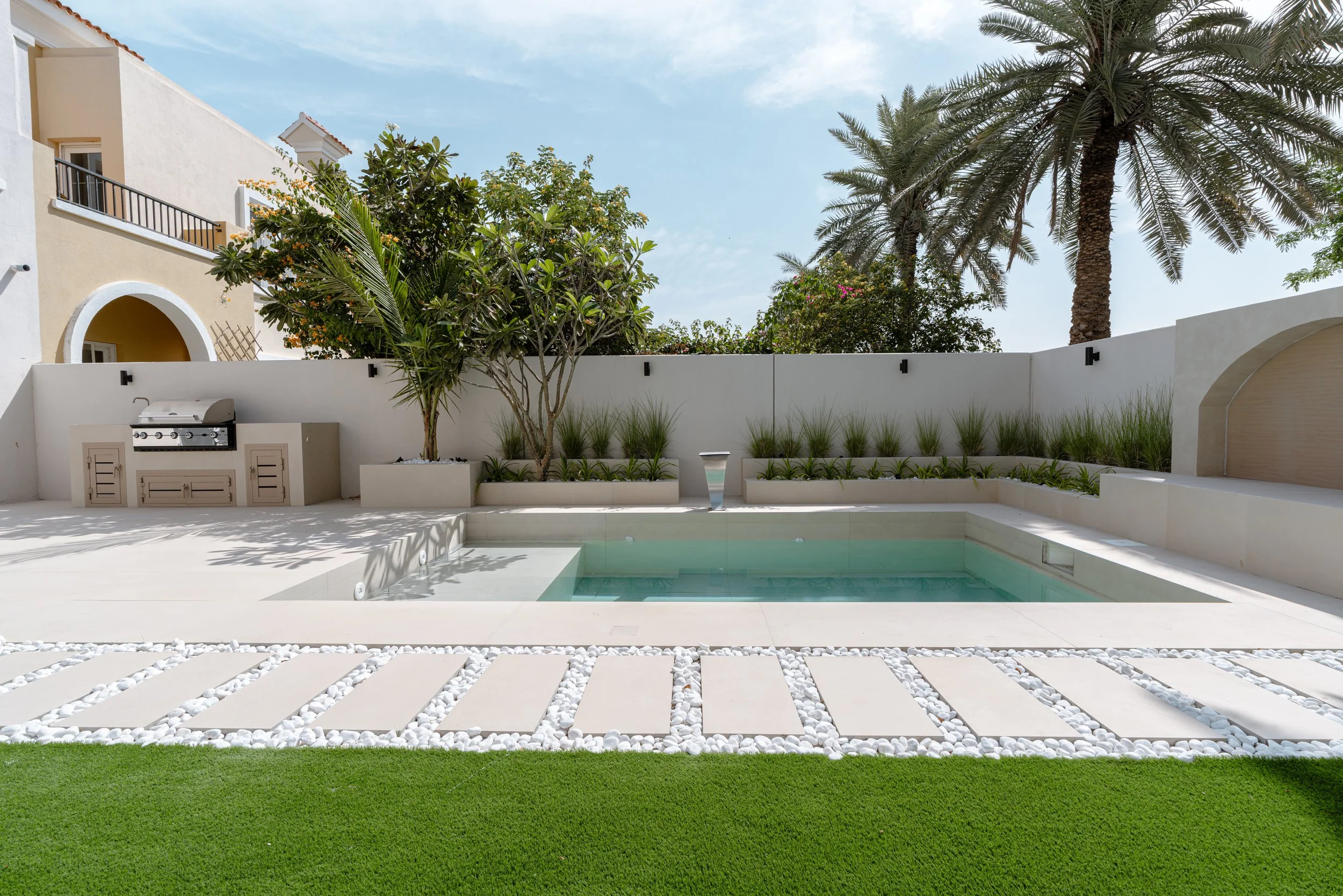 Villa garden with swimming pool, lawn, stepping stones, planter beds and palm trees.