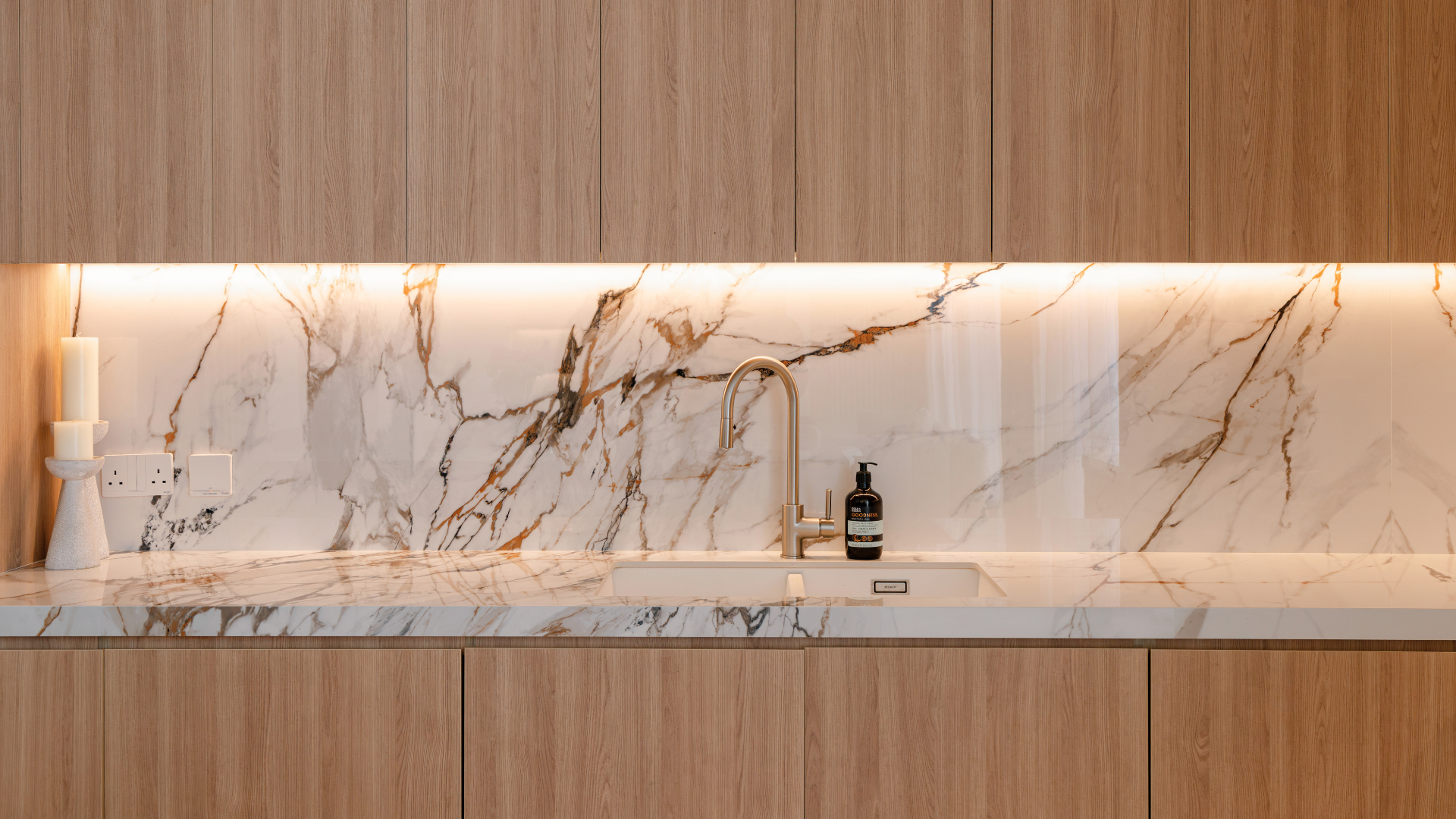 Bespoke wood kitchen cabinetry with illuminated marble backsplash and brass tap in a Tilal Al Furjan villa.