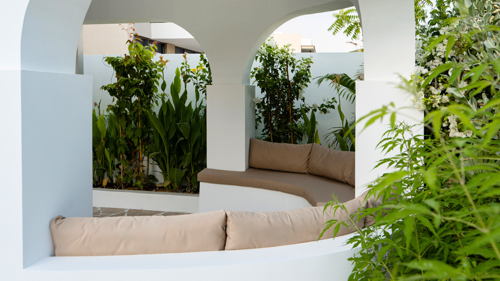 Curved outdoor seating beneath a sculptural arched pavilion surrounded by lush garden planting.