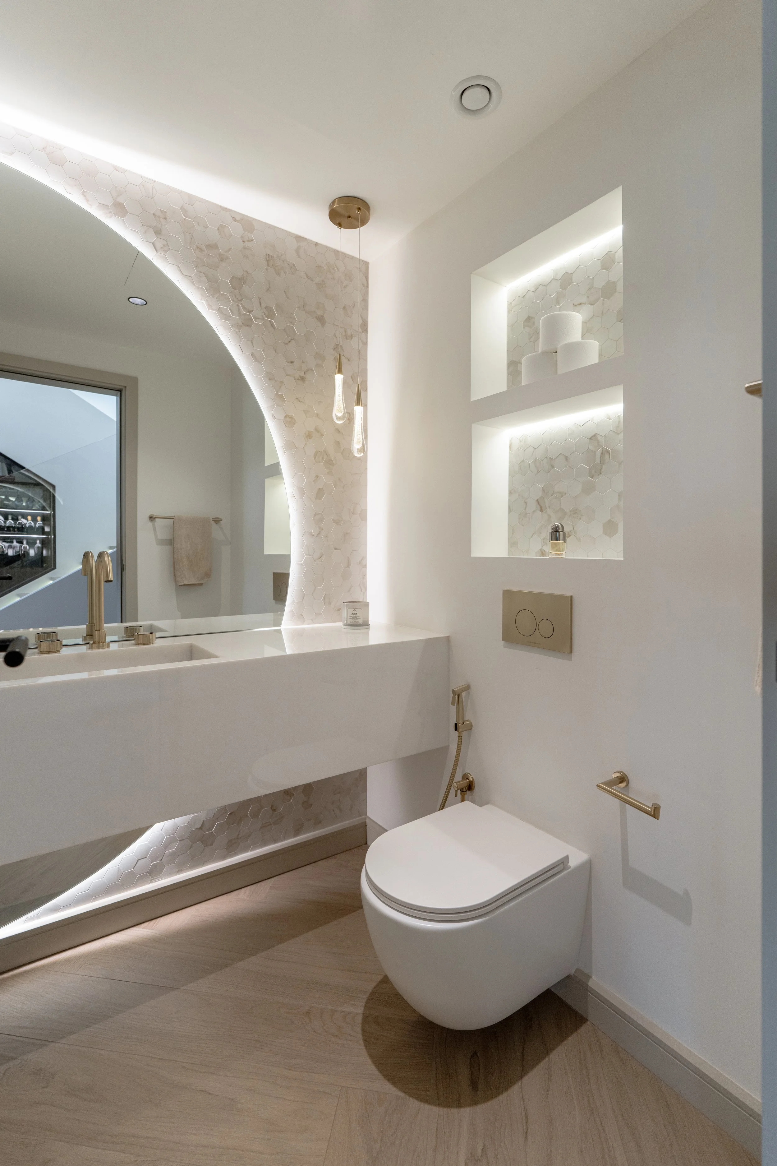 Renovated bathroom with stone vanity, arched mirror, wall niche lighting and brass fixtures.