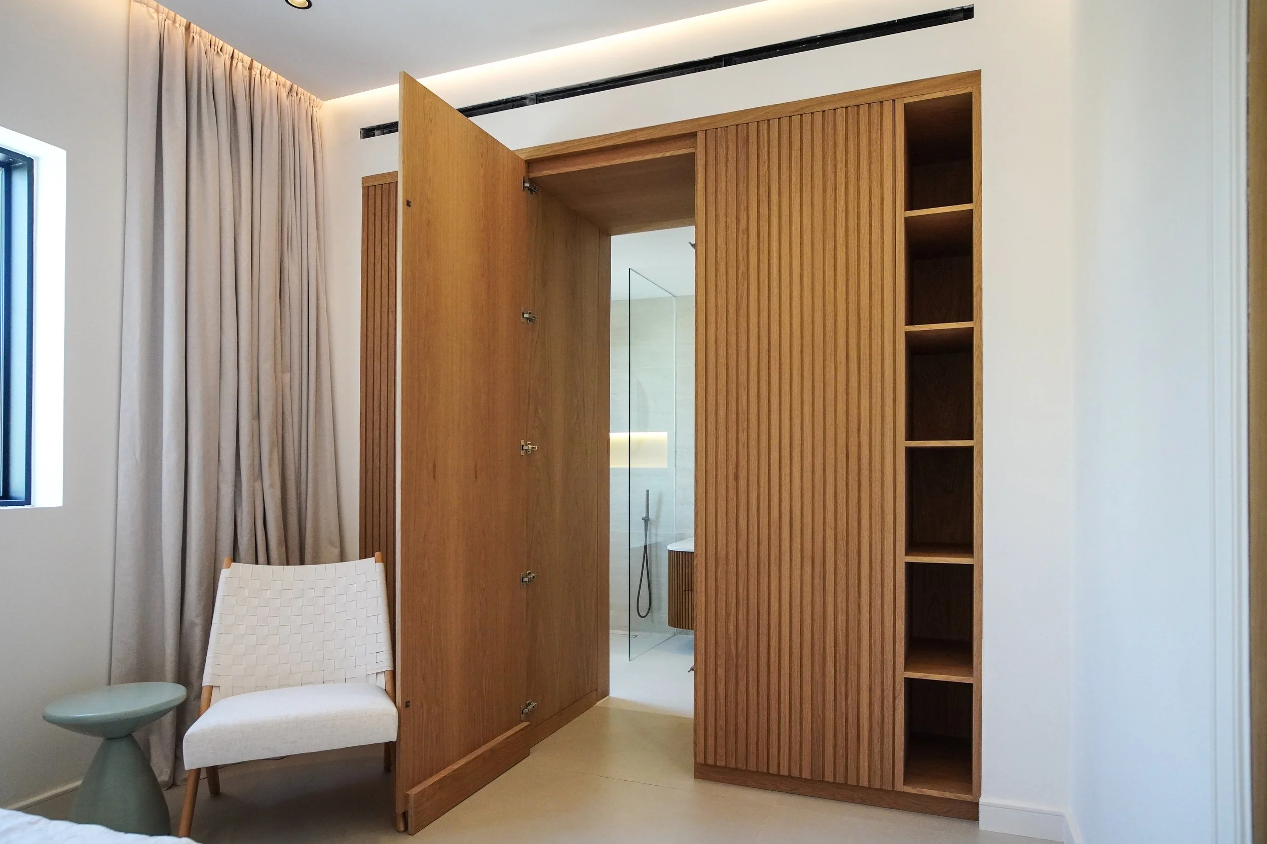Custom wood wardrobe and concealed bathroom door with fluted panels in a villa bedroom.