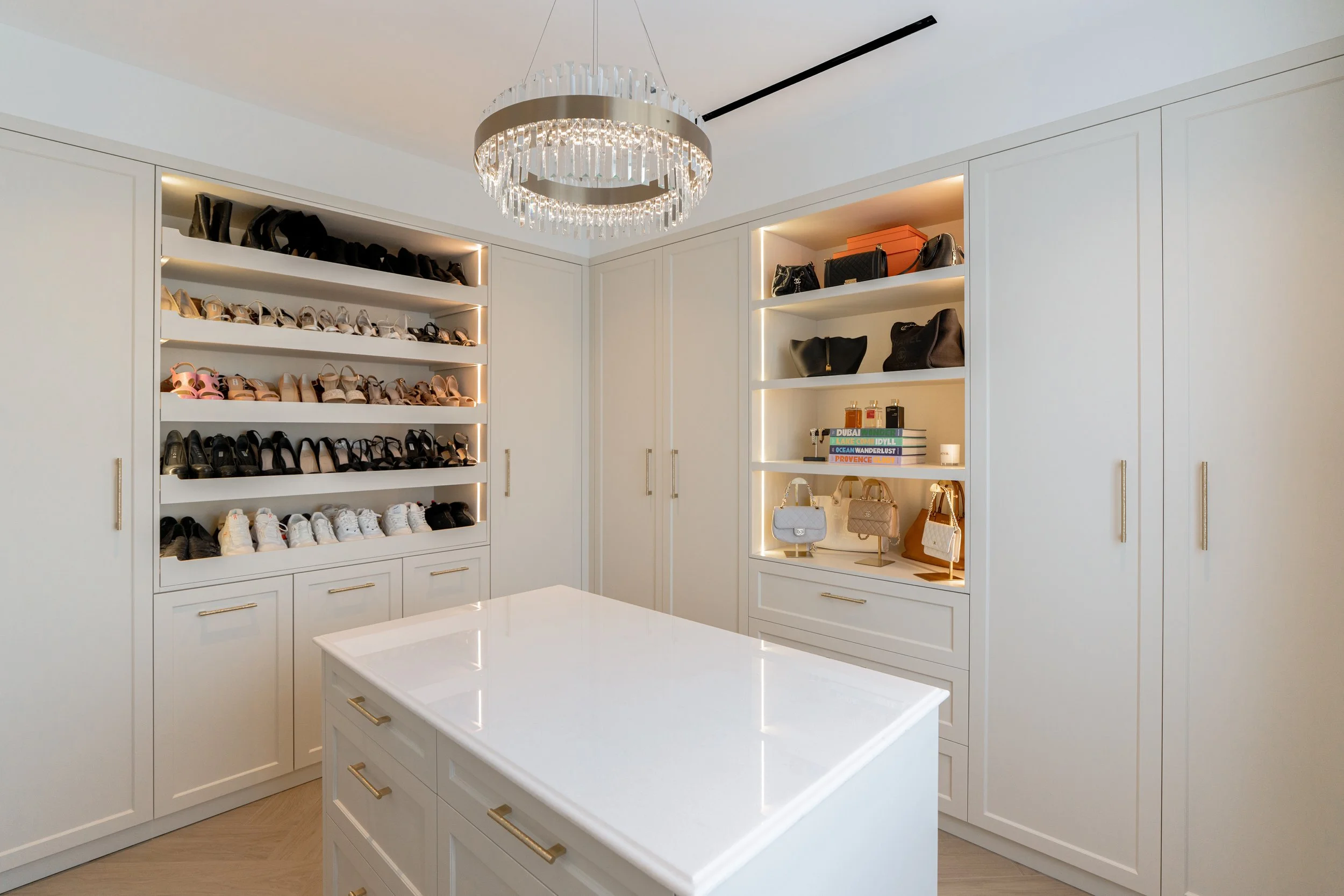 Custom dressing room with illuminated shoe shelves, handbag display, fitted wardrobes and central island.