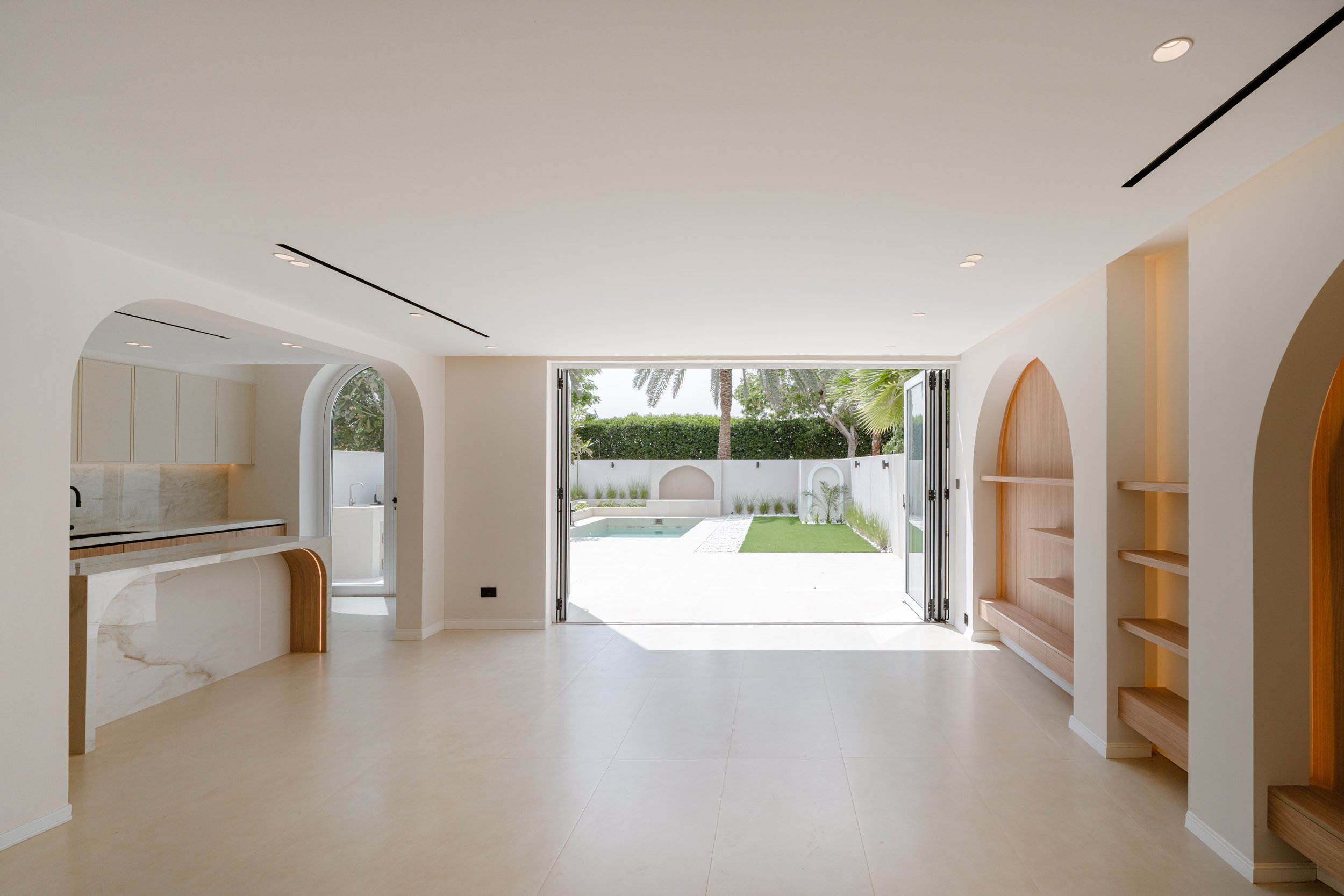 Open-plan Al Reem 1 villa living and kitchen area with arched joinery, garden access and neutral finishes.