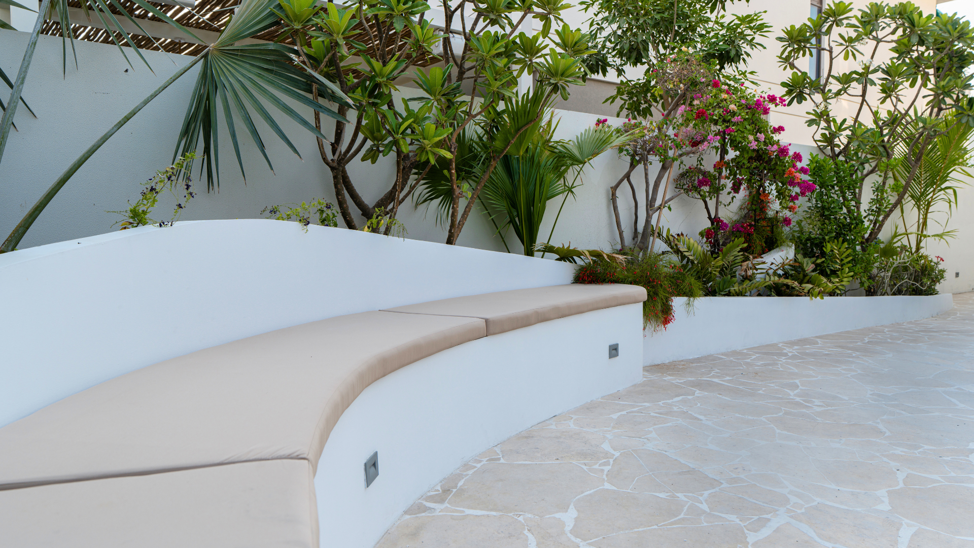 Curved built-in garden seating surrounded by palms and flowering plants in a Dubai villa landscape.