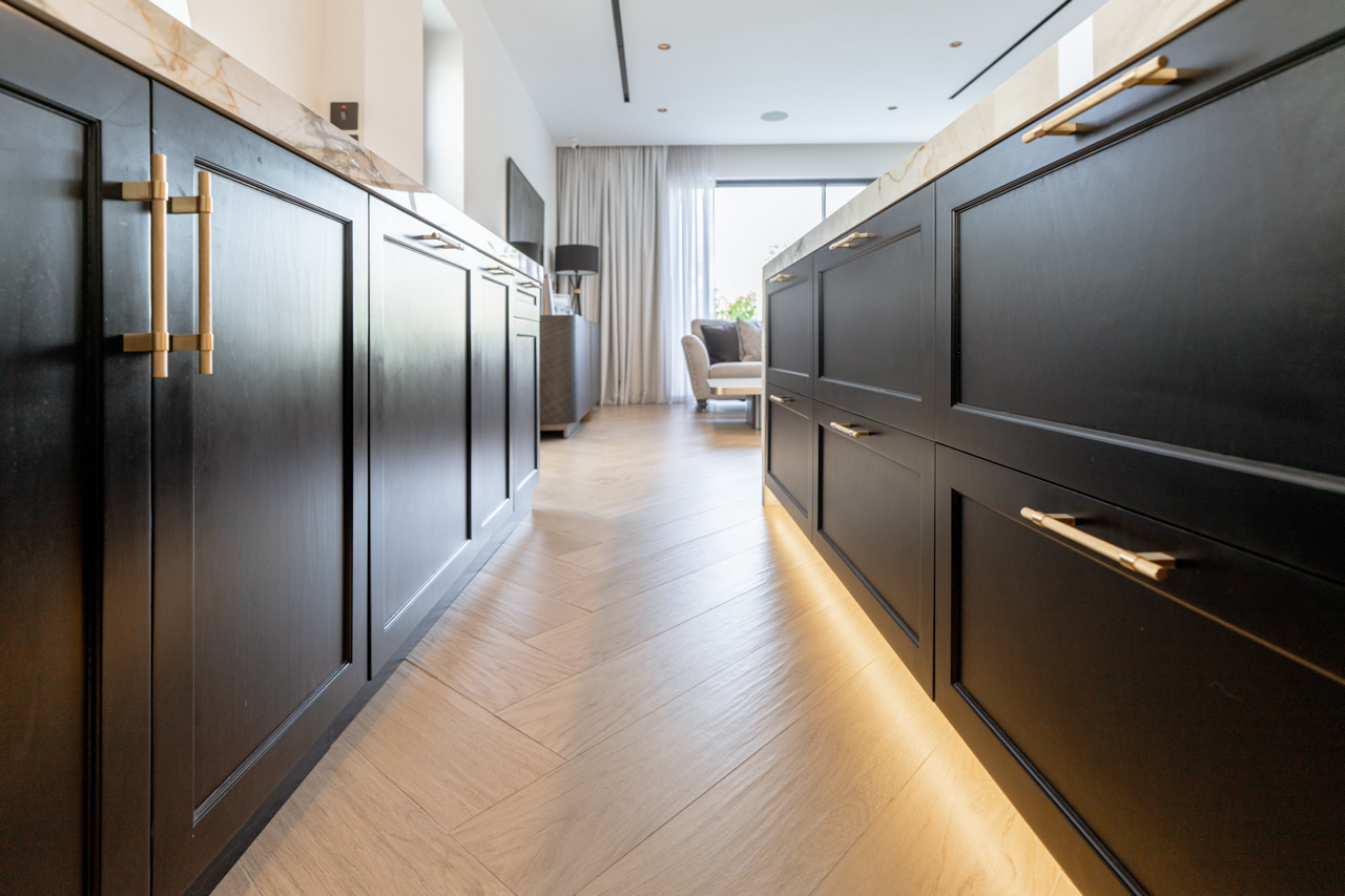 Custom black kitchen cabinetry with brass handles and integrated lighting in a renovated villa.