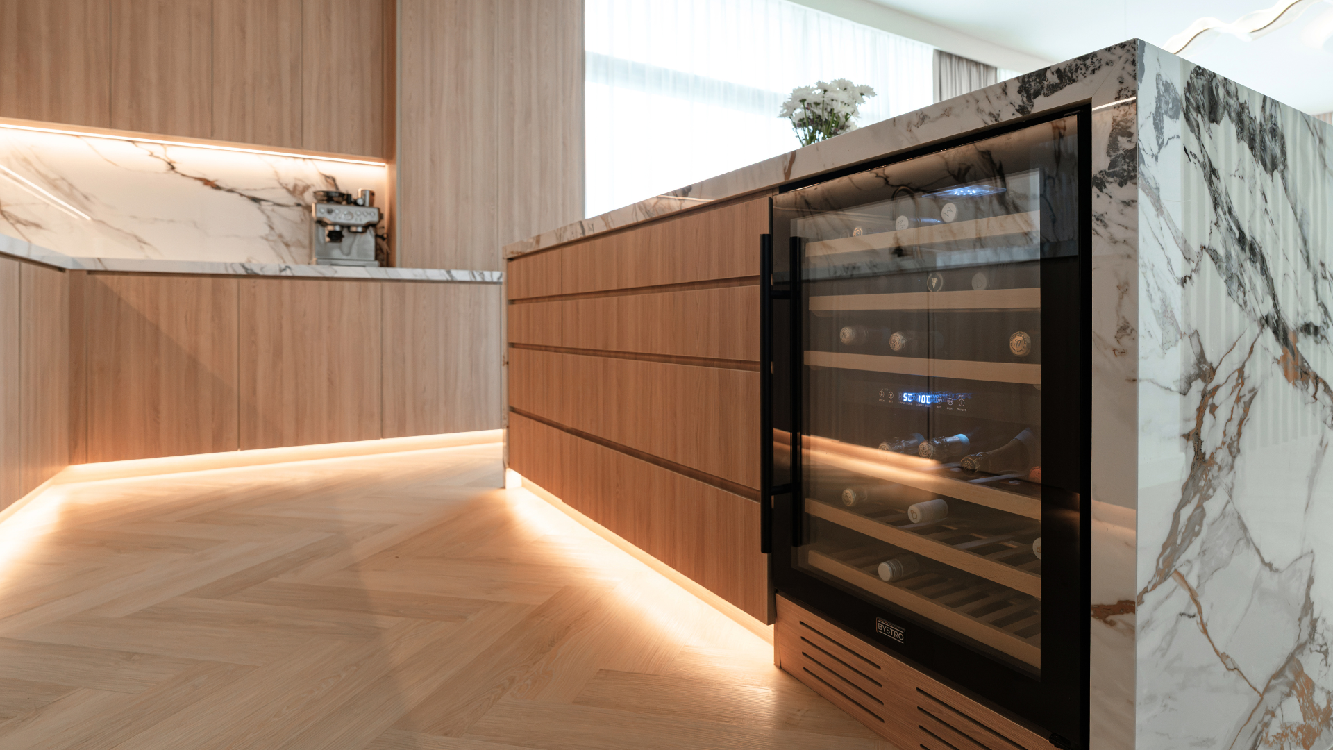Marble kitchen island with integrated wine fridge, wood panelling and concealed lighting in a Dubai villa.