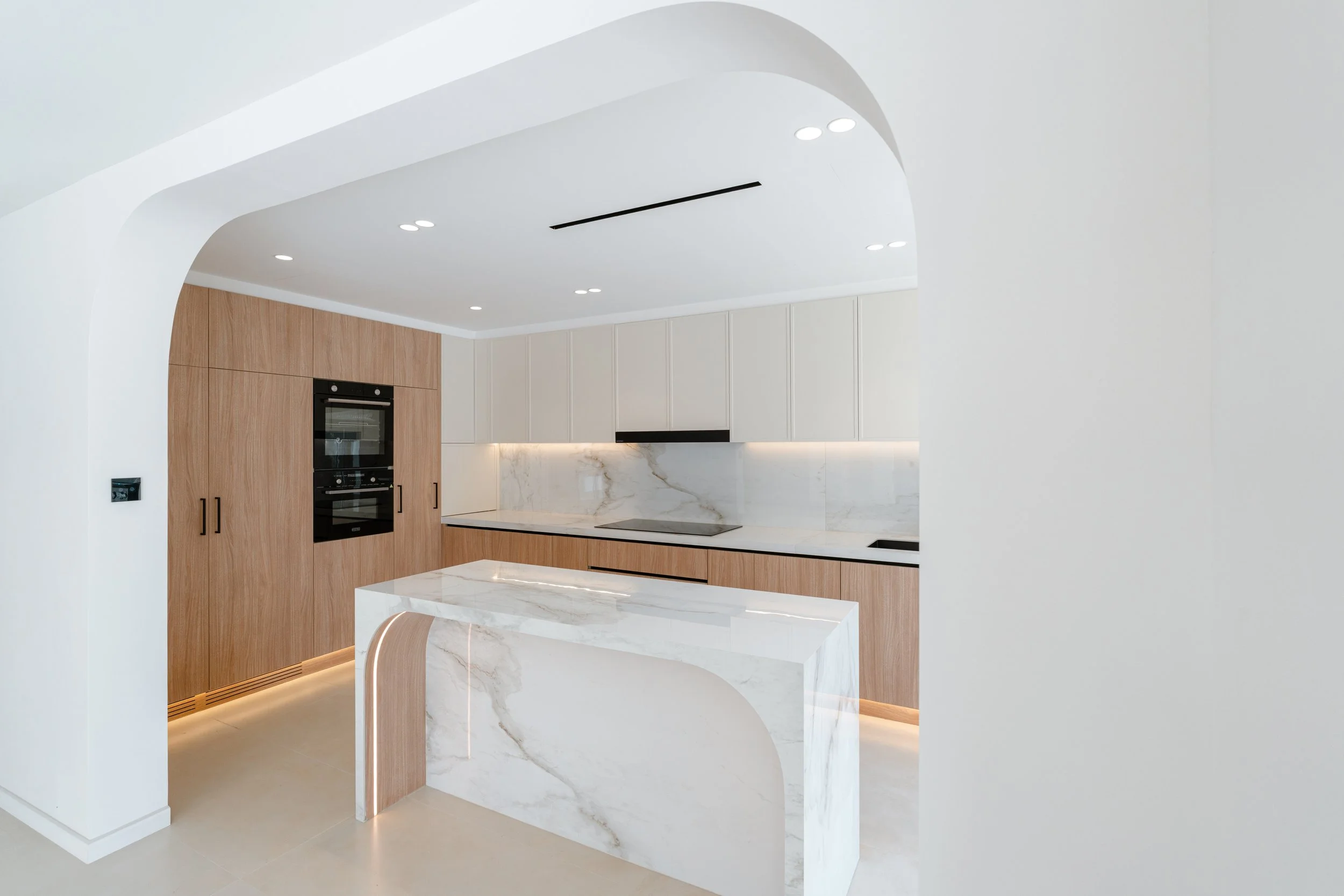 Al Reem 1 villa kitchen with marble island, timber cabinetry, arched opening and integrated lighting.