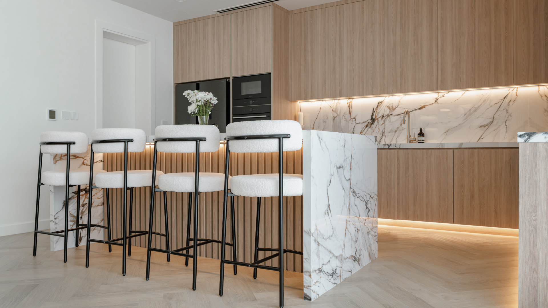 Bespoke kitchen island with marble waterfall edge, bar seating and integrated appliances.