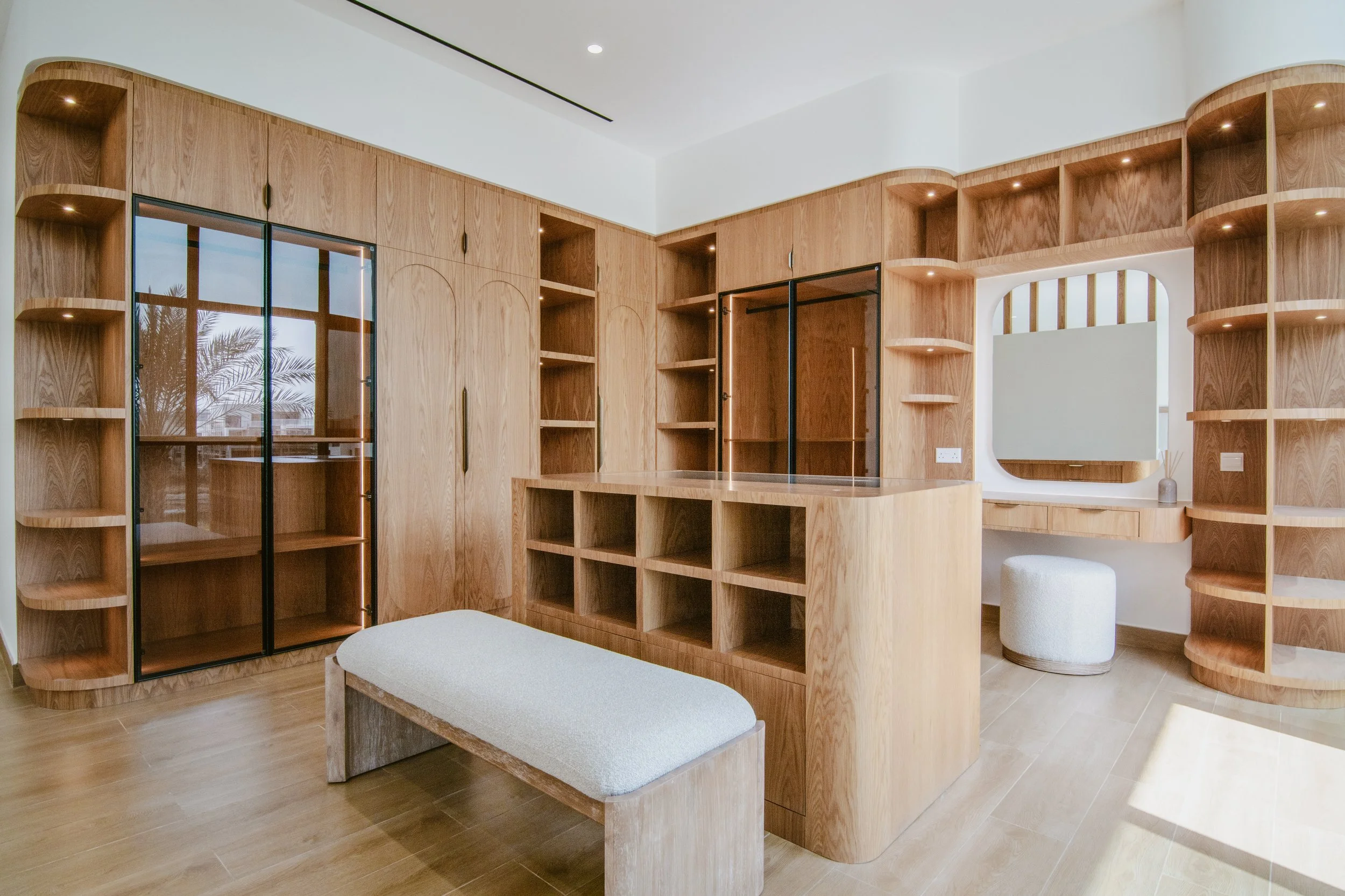 Bespoke dressing room with custom wood wardrobes, glass doors, vanity area and central bench.