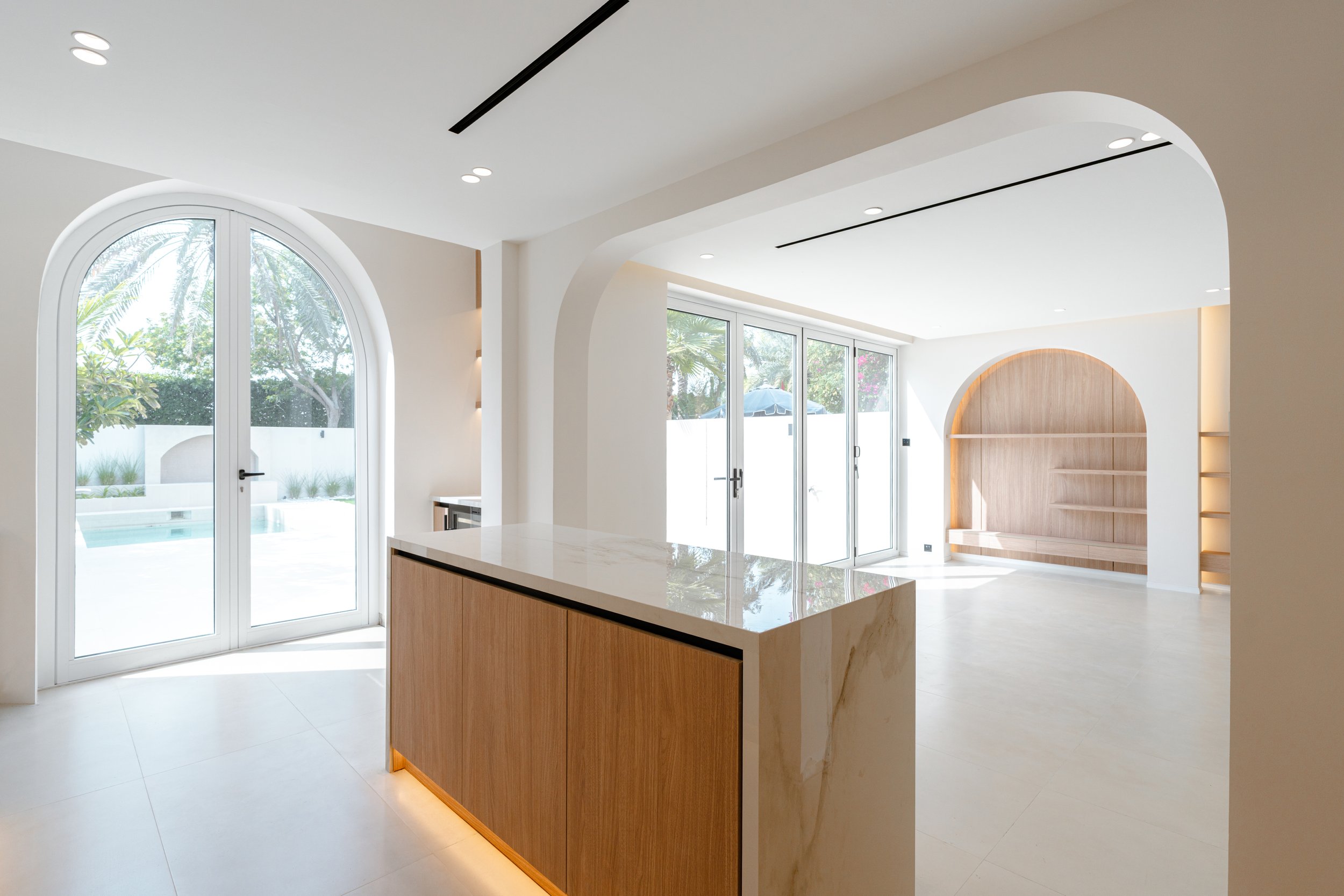 Al Reem 1 villa kitchen with marble island, timber cabinetry, arched opening and integrated lighting.