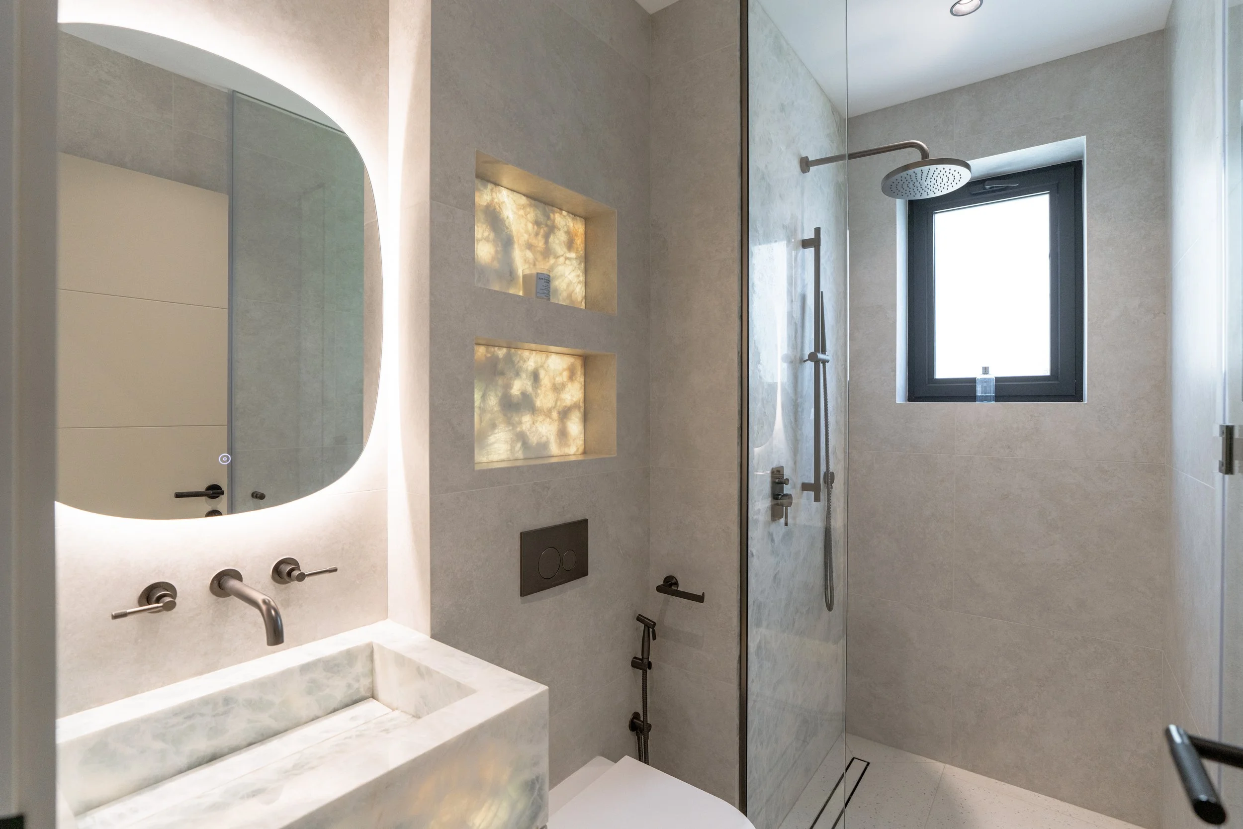 Renovated bathroom with stone vanity, arched mirror, wall niche lighting and brass fixtures.