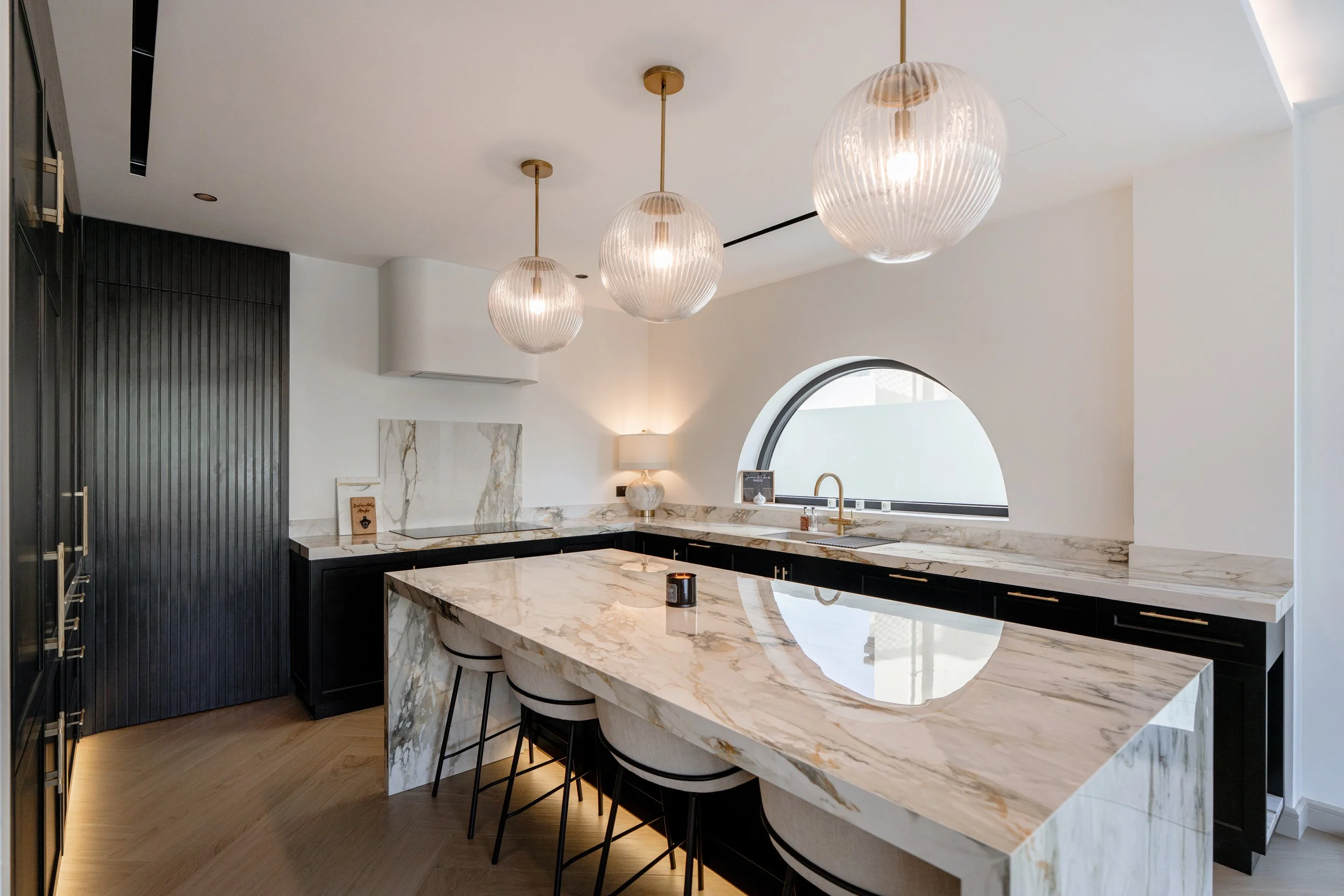 Jumeirah Park villa kitchen with marble island, pendant lighting, arched window and bar seating.