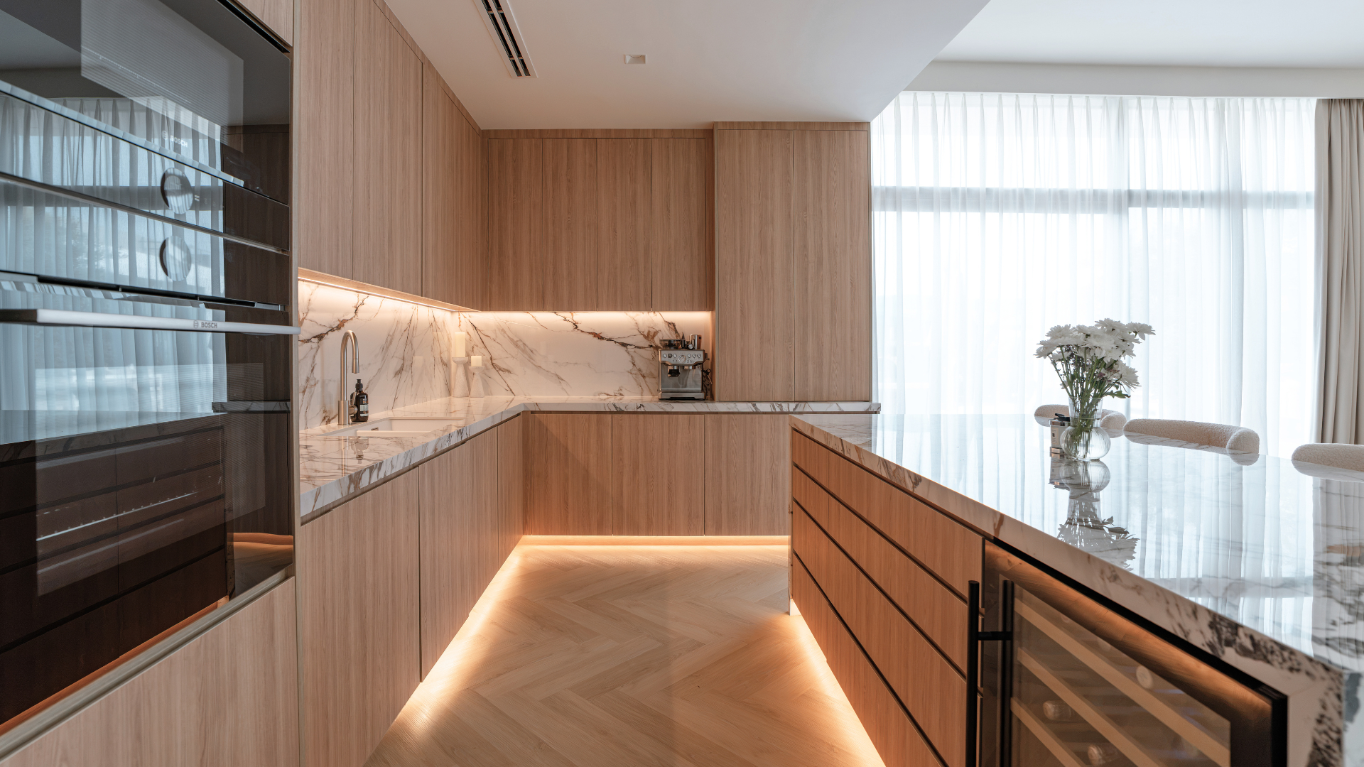 Bespoke handleless kitchen with wood cabinetry, marble worktops, wine fridge and integrated lighting.