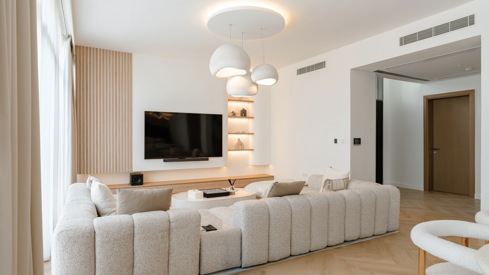 Neutral Dubai villa living room with curved sectional seating, statement pendant lights and custom media wall.