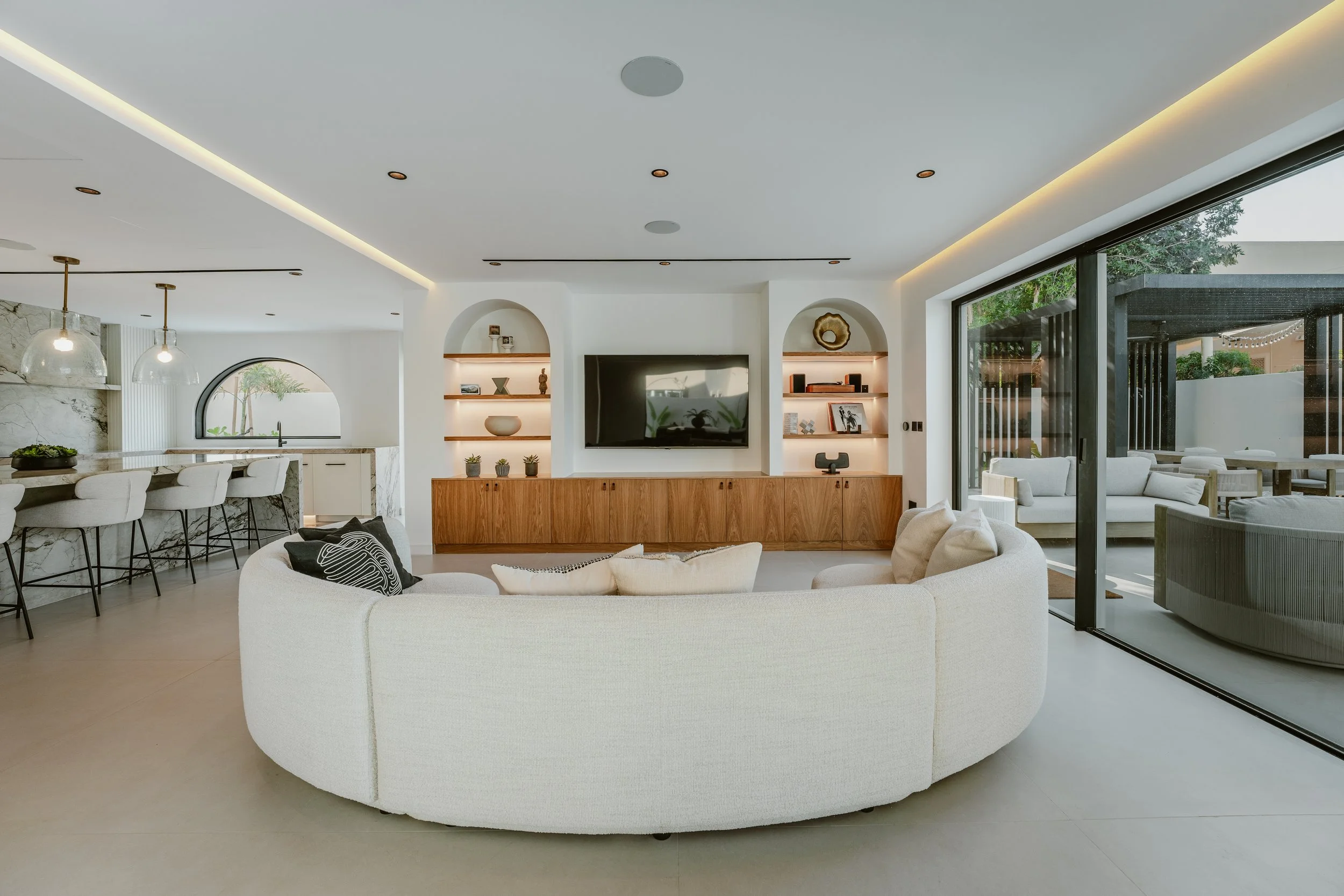 Al Mahra villa lounge with curved sofa, custom media wall, open shelving and garden access.