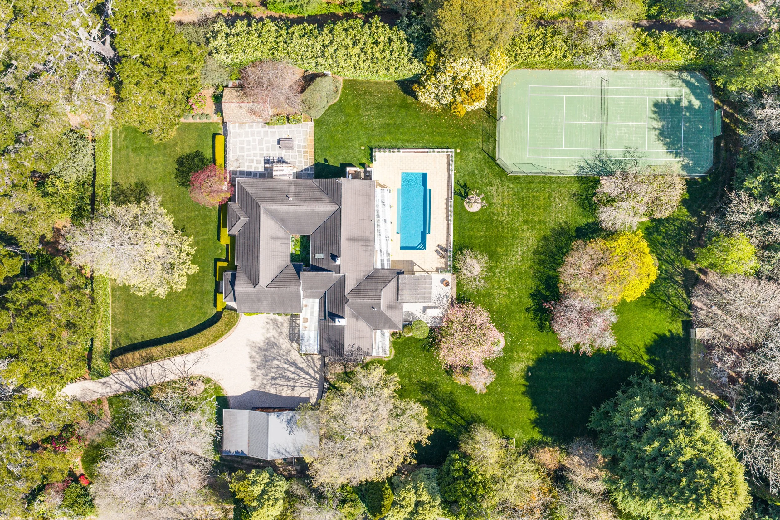 Aerial view of a large residential backyard with a house, swimming pool, tennis court, and various trees and greenery.