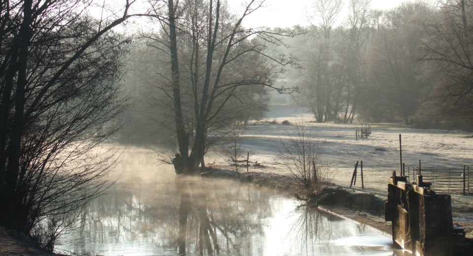 Early morning view of the mill stream in Rix, with frost-covered ground and mist rising in the soft winter light, capturing the peaceful countryside atmosphere.