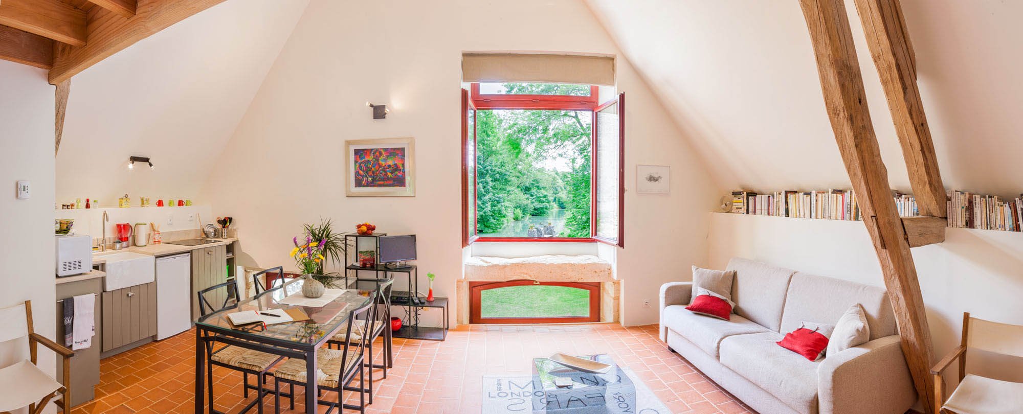 Panoramic interior of a bright holiday gite at Rix Mill in Burgundy, featuring exposed oak beams, terracotta floors, and a large window overlooking a river.