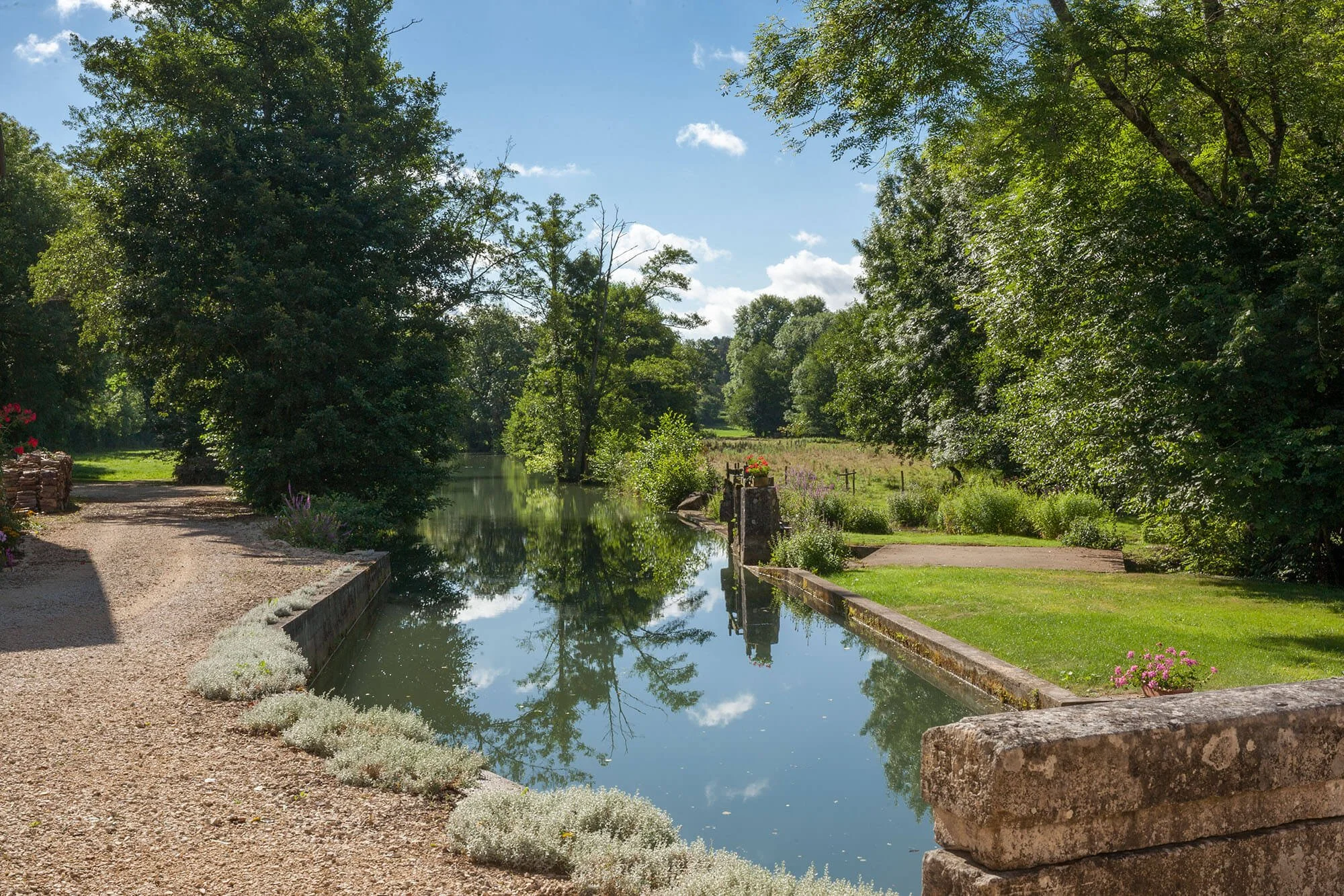 The tranquil mill pond at Rix Mill, reflecting trees, meadow and stonework in the heart of the Burgundy countryside.