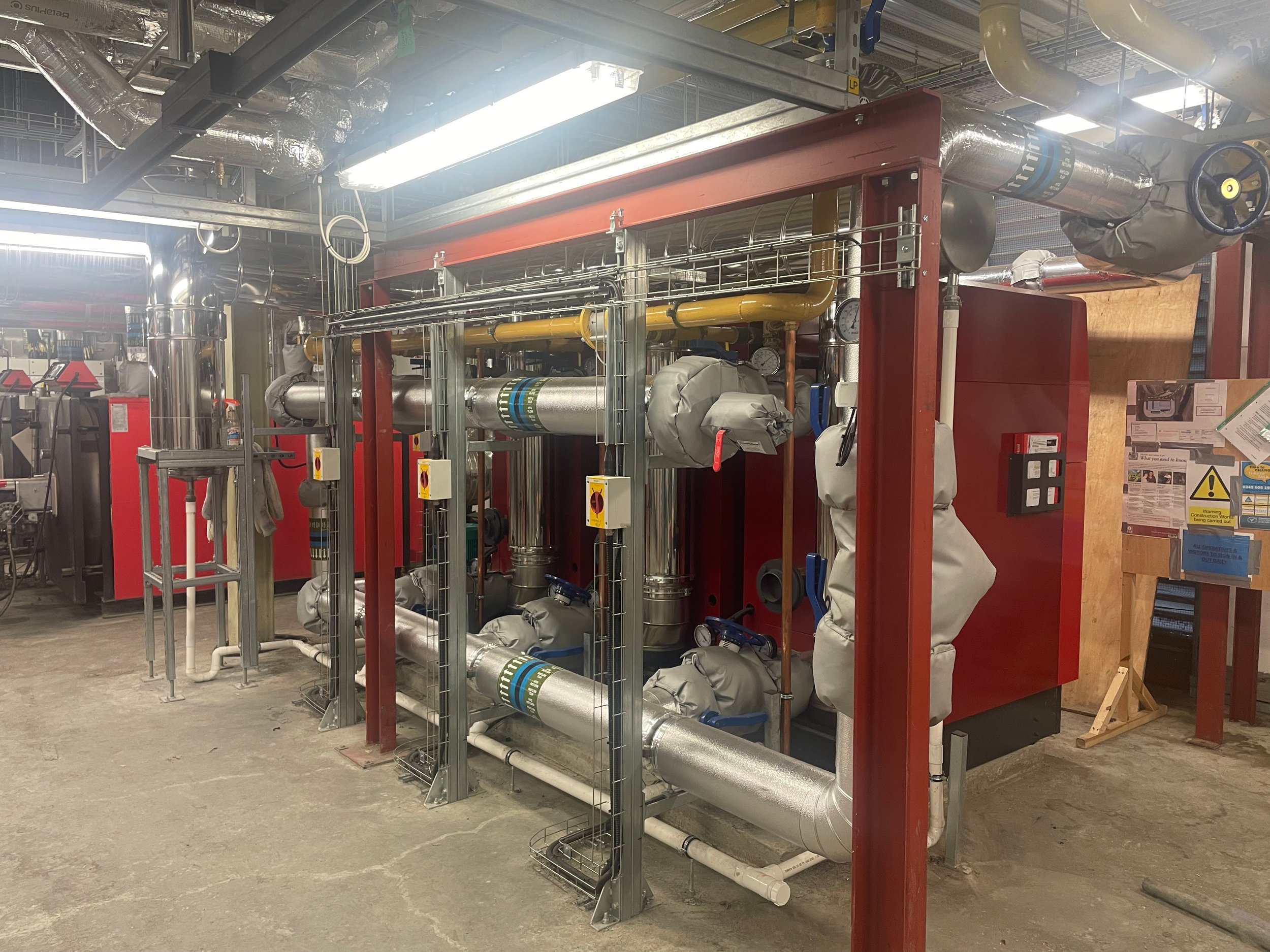 Industrial heating system with metallic pipes, valves, and insulation within a facility.