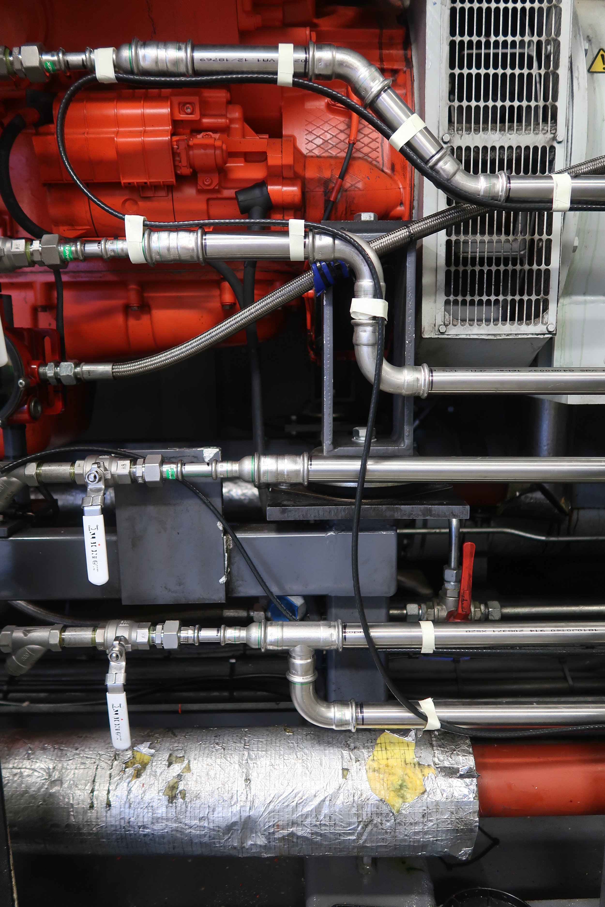 Close-up view of machinery with various metal pipes, fittings, and labels, part of an industrial system.