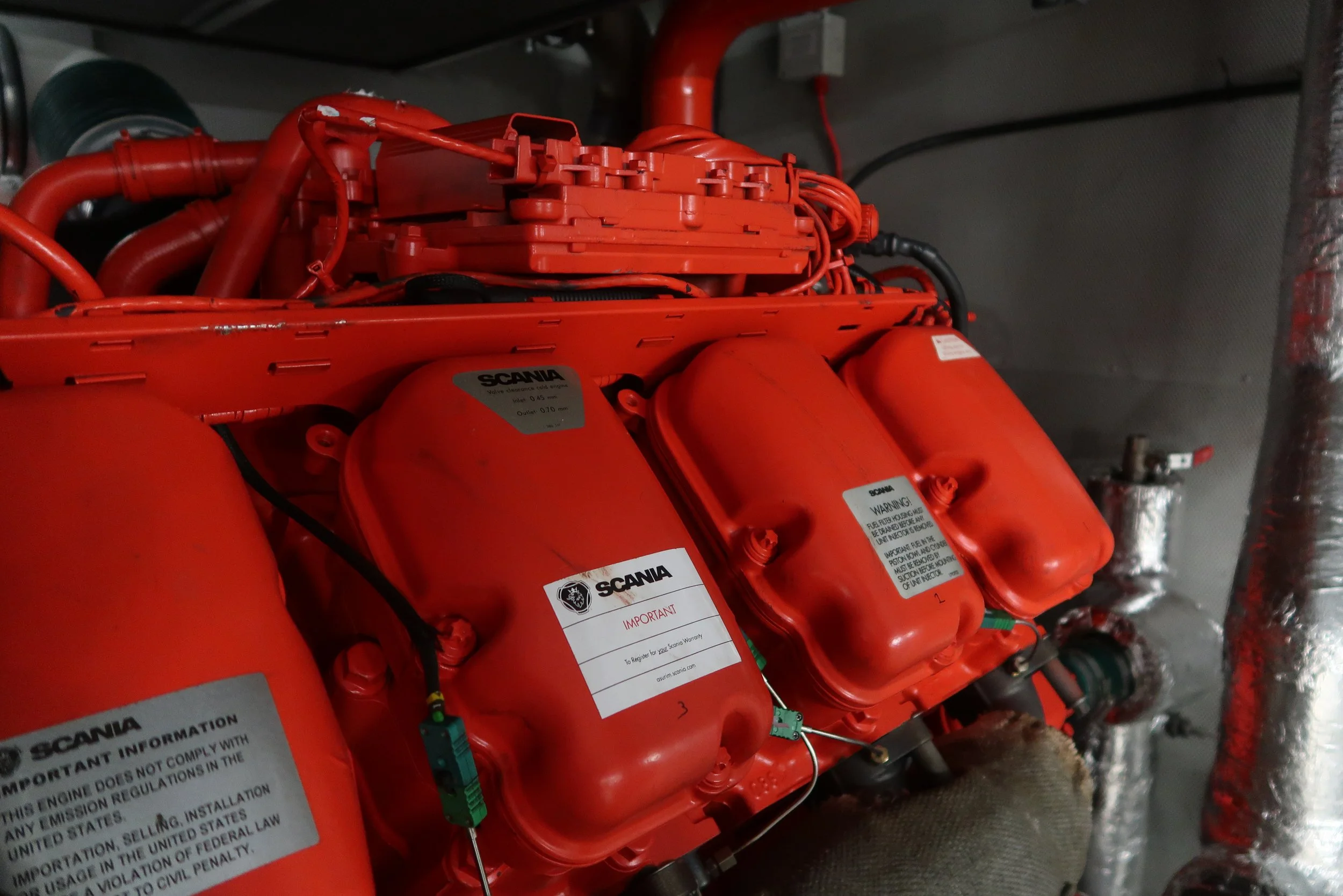 Red industrial engine or pump system with warning labels and wiring, located in an indoor facility with insulated pipes.