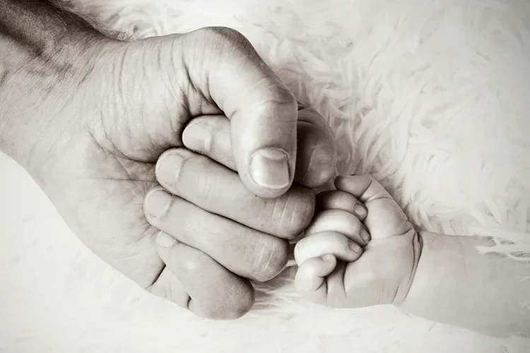 Black and white photo, an adult fist next to a baby fist