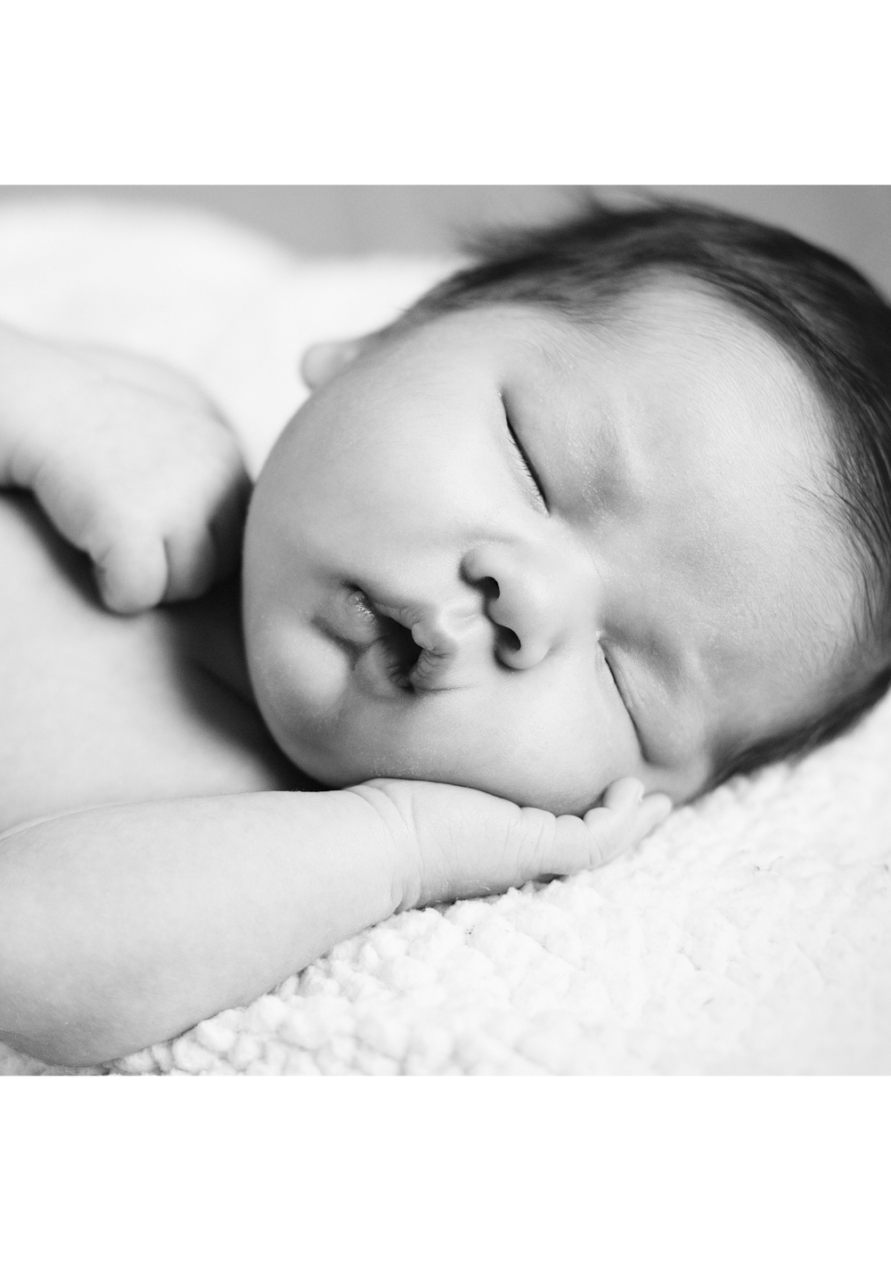A black and white close-up photo of a sleeping baby with a hand gently supporting their face.