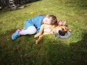 A young girl lying on the grass hugging a small dog, both relaxing outdoors.
