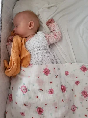 Young baby peacefully sleeping on a bed, wrapped in a floral blanket, with a small cloth in hand.