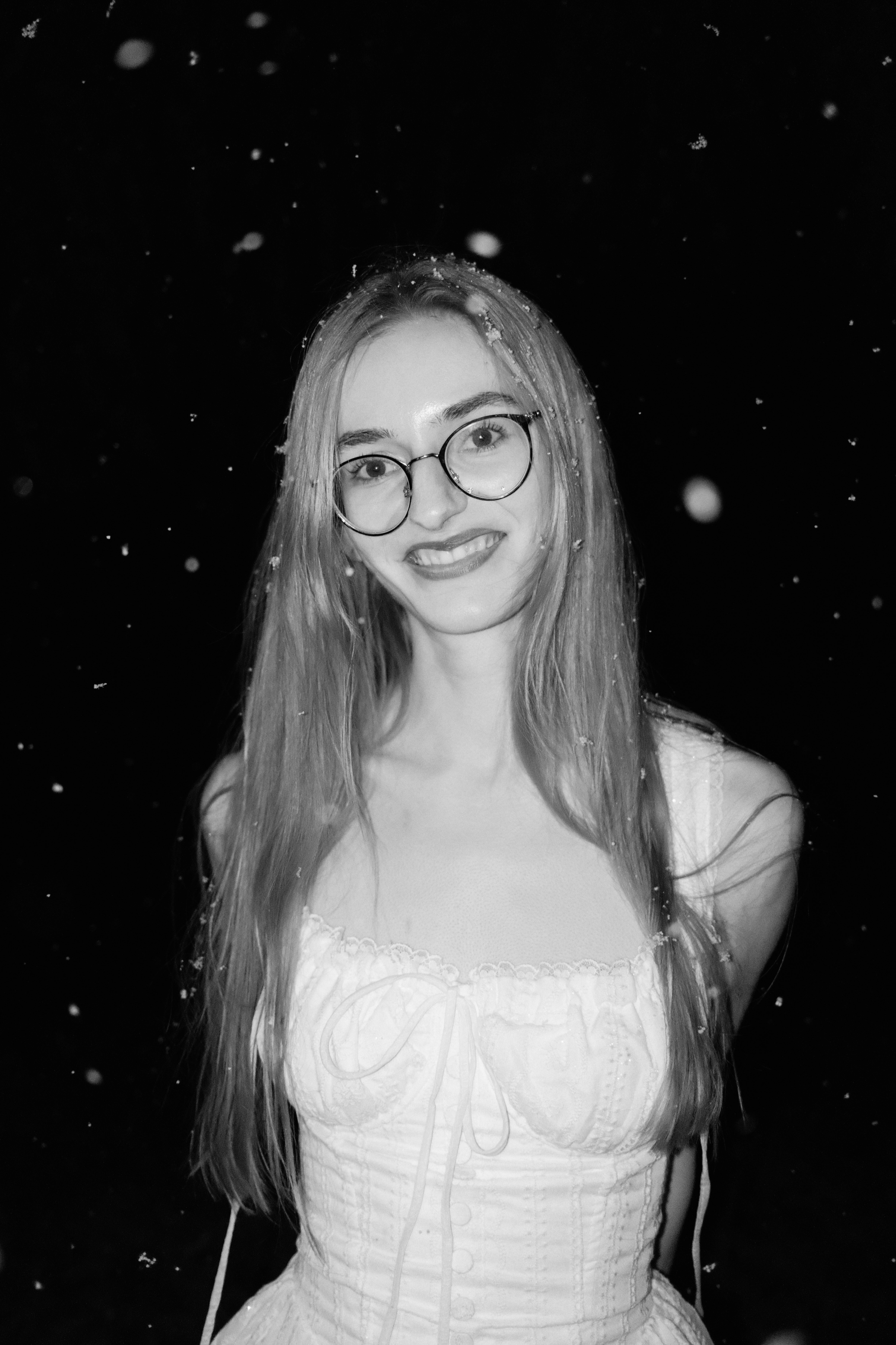 Schwarz-weiß Foto eines lachenden Mädchens (Jasmin Peter) mit Brille, das im Freien bei Schneefall steht.