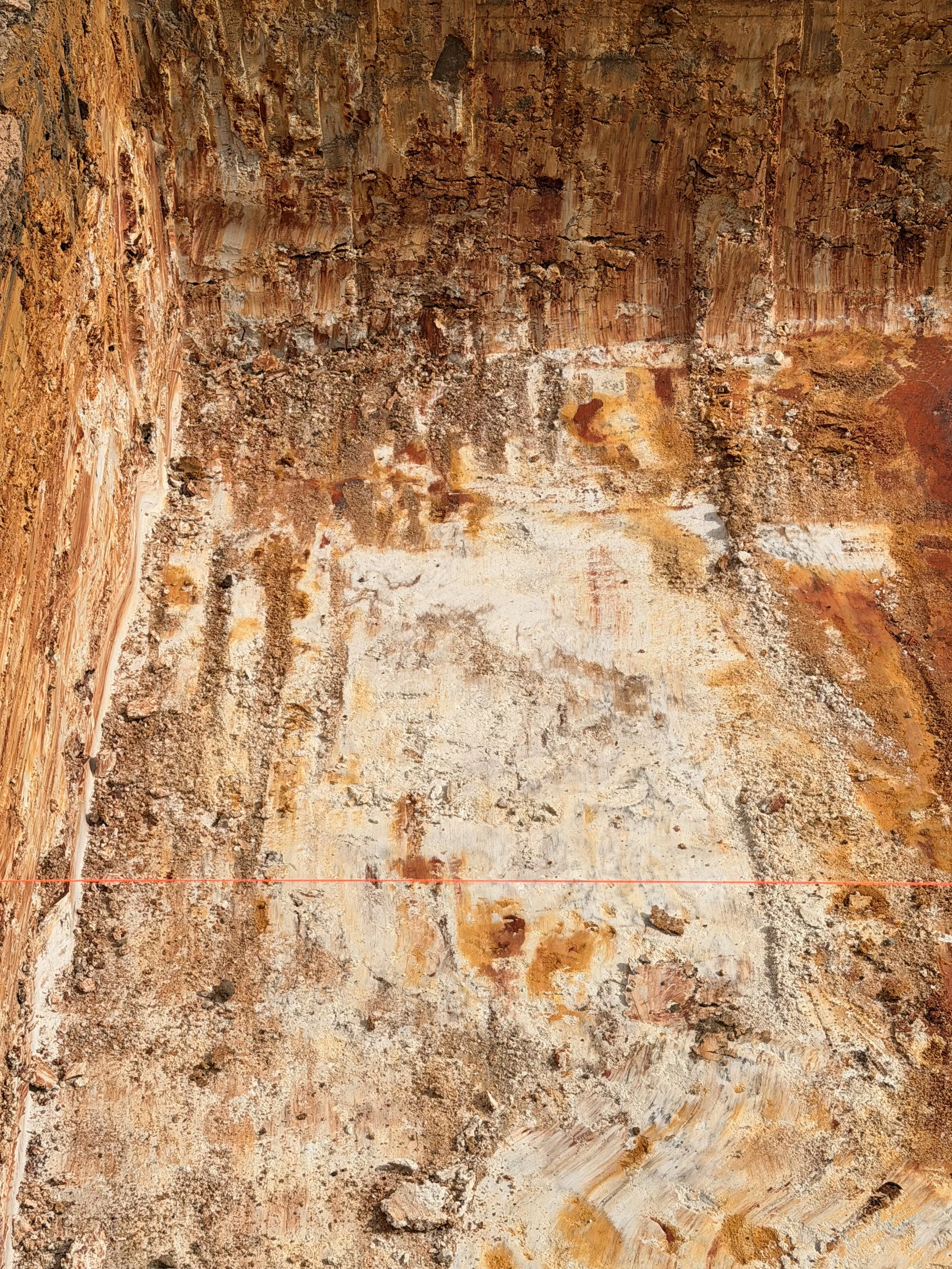 Close-up view of a textured, rusty, and weathered wall or surface with earthy tones of orange, brown, and beige.
