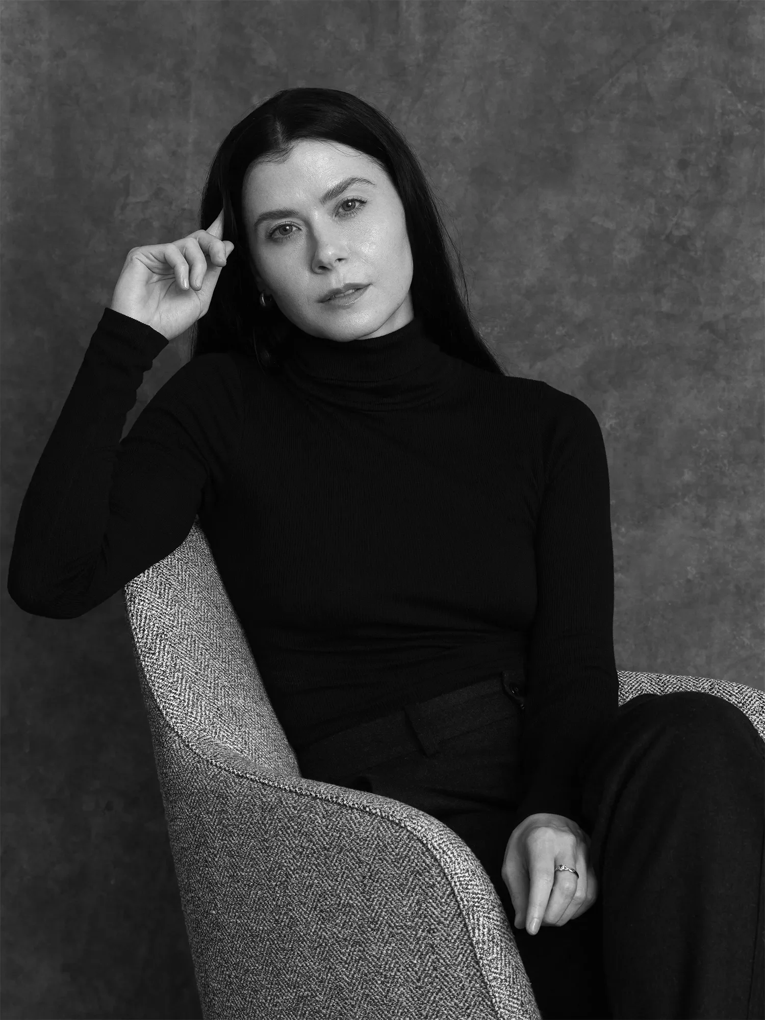 Black and white photo of Dr Stephanie Knight, a Chartered Counselling Psychologist with dark hair, wearing a black turtleneck, seated in an armchair, with a textured background behind her.