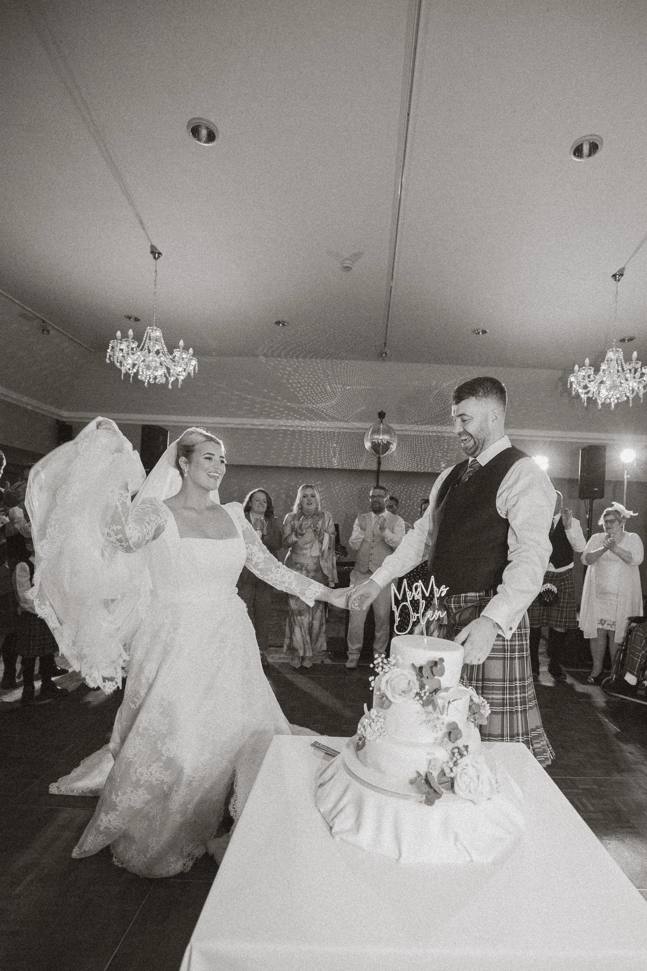 Bride and groom dancing at their wedding reception with wedding cake on table in front.