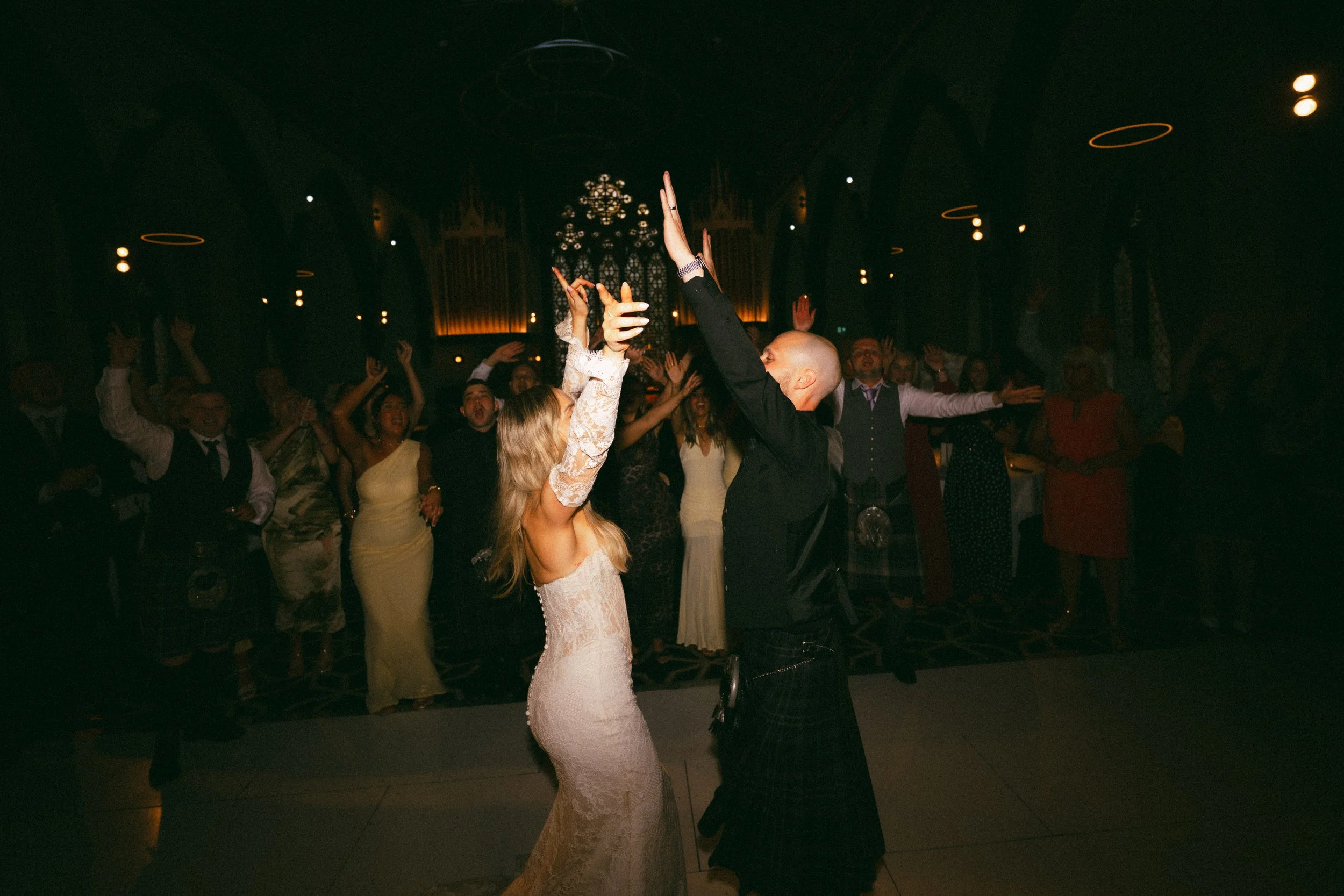 A couple dancing at a wedding reception, surrounded by guests in a dimly lit banquet hall.