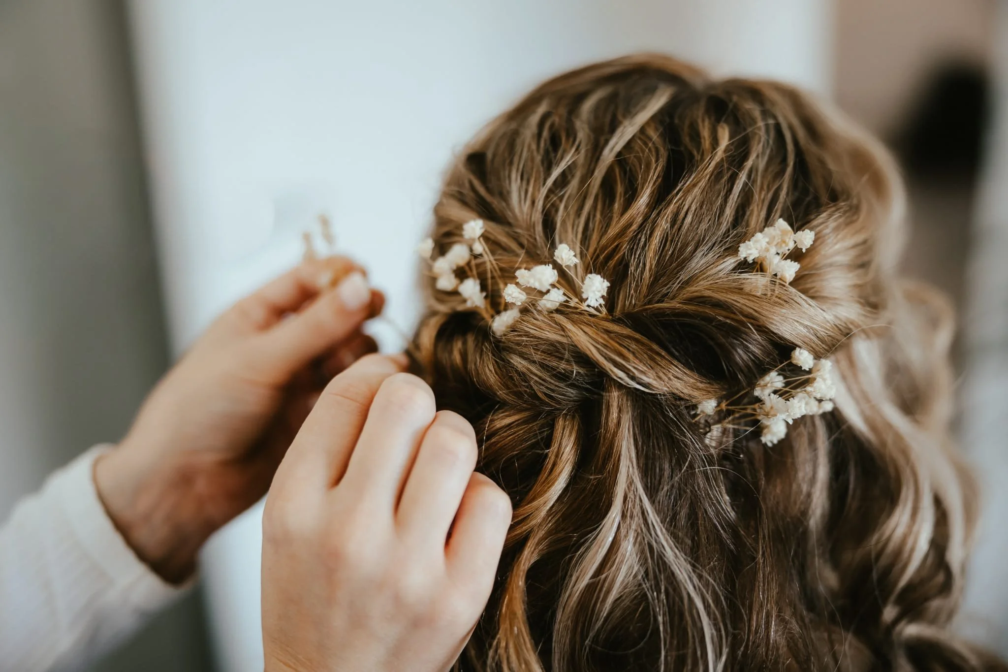 Close-up of a person styling a woman's braided hair with small white flowers.
