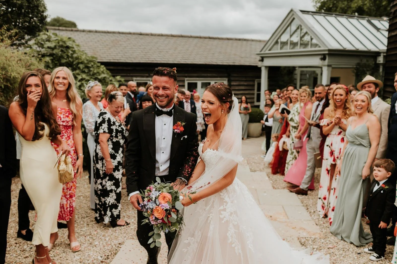 Happy bride and groom surrounded by wedding guests celebrating outdoors.