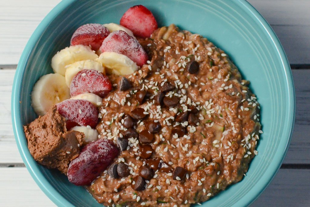 A bowl of oatmeal topped with chocolate chips, chopped nuts, sliced bananas, sliced strawberries, and a spoonful of peanut butter on the side.