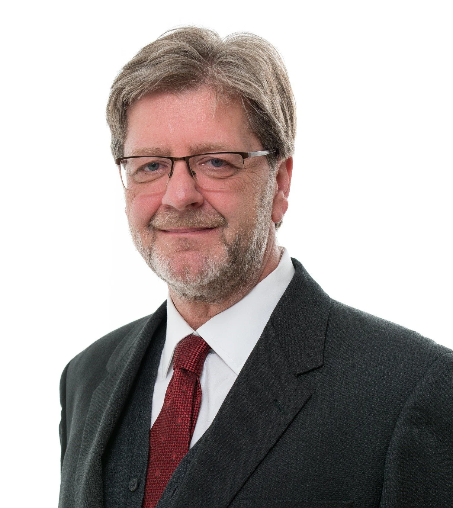 A middle-aged man wearing a black suit, white shirt, red tie, and glasses, smiling against a plain white background.