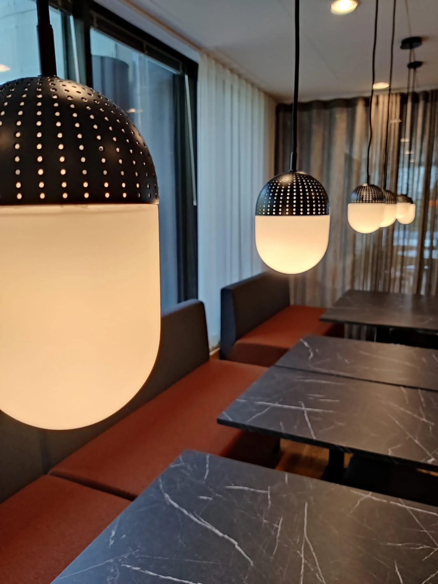 Ravintolassa musta marmorikuvioitu pöytä ja oranssit sohvat, riippuvalaisimet